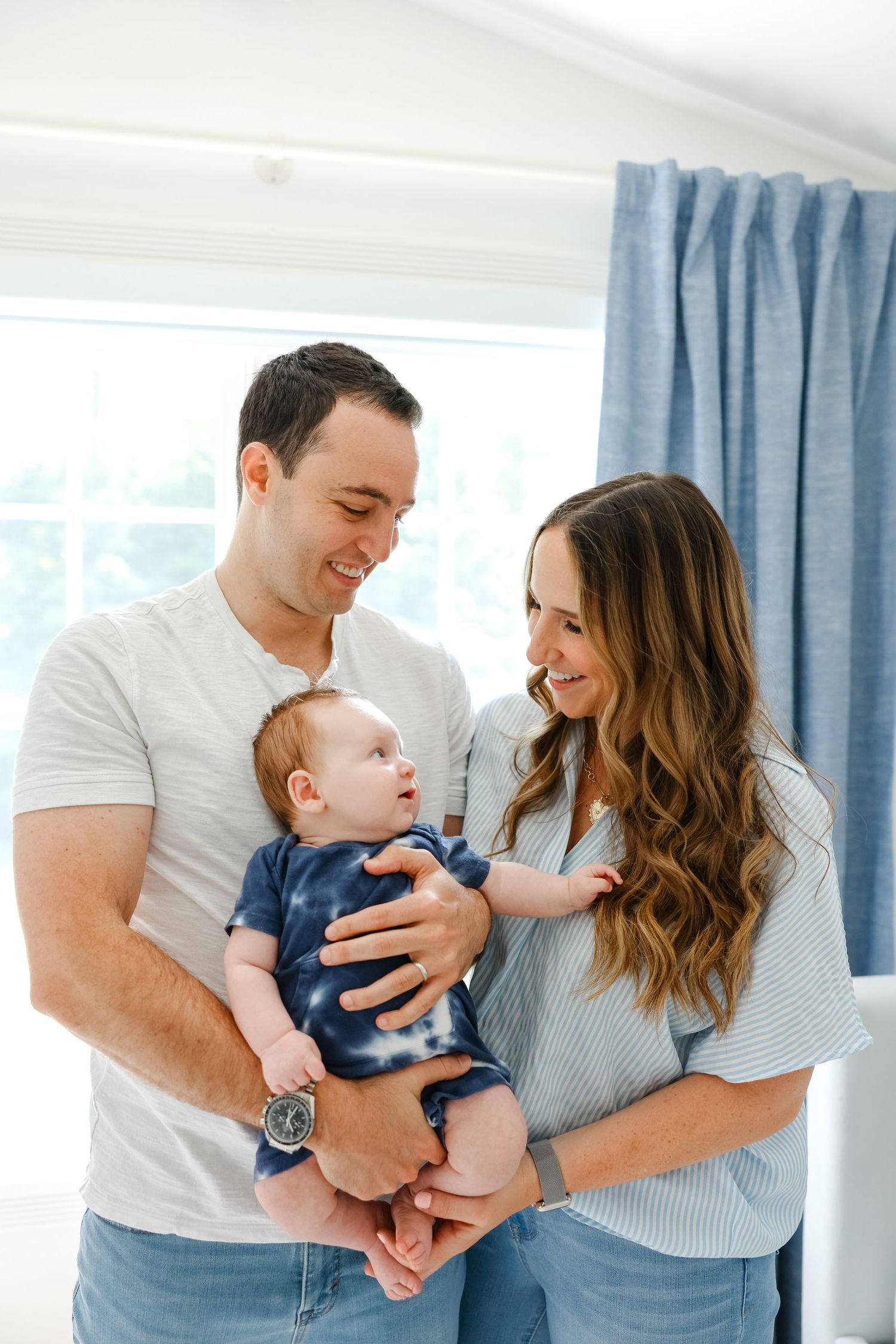 A bright indoor photo of a happy family of three sharing a joyful moment together in a sunlit room.