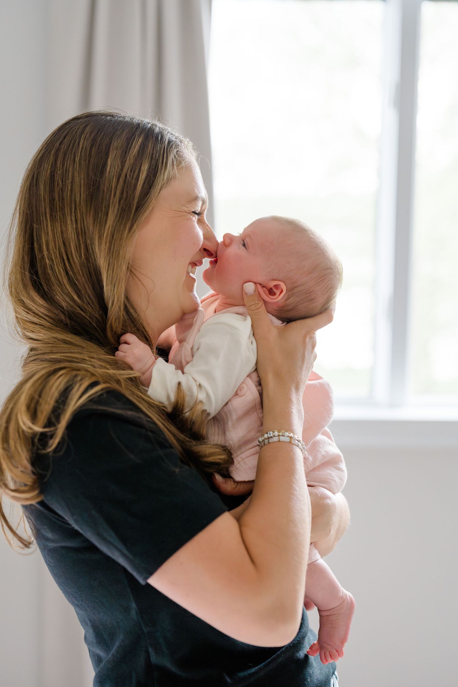 A parent shares tender nose-to-nose moments with their newborn baby in a bright indoor setting.
