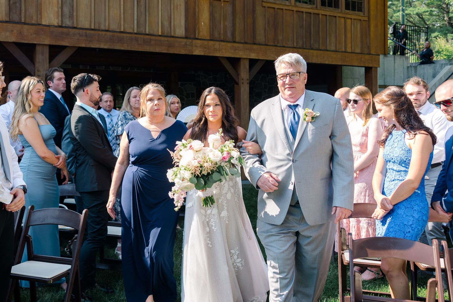 Wedding ceremony with a couple walking down the aisle while guests in navy blue and floral dresses look on.