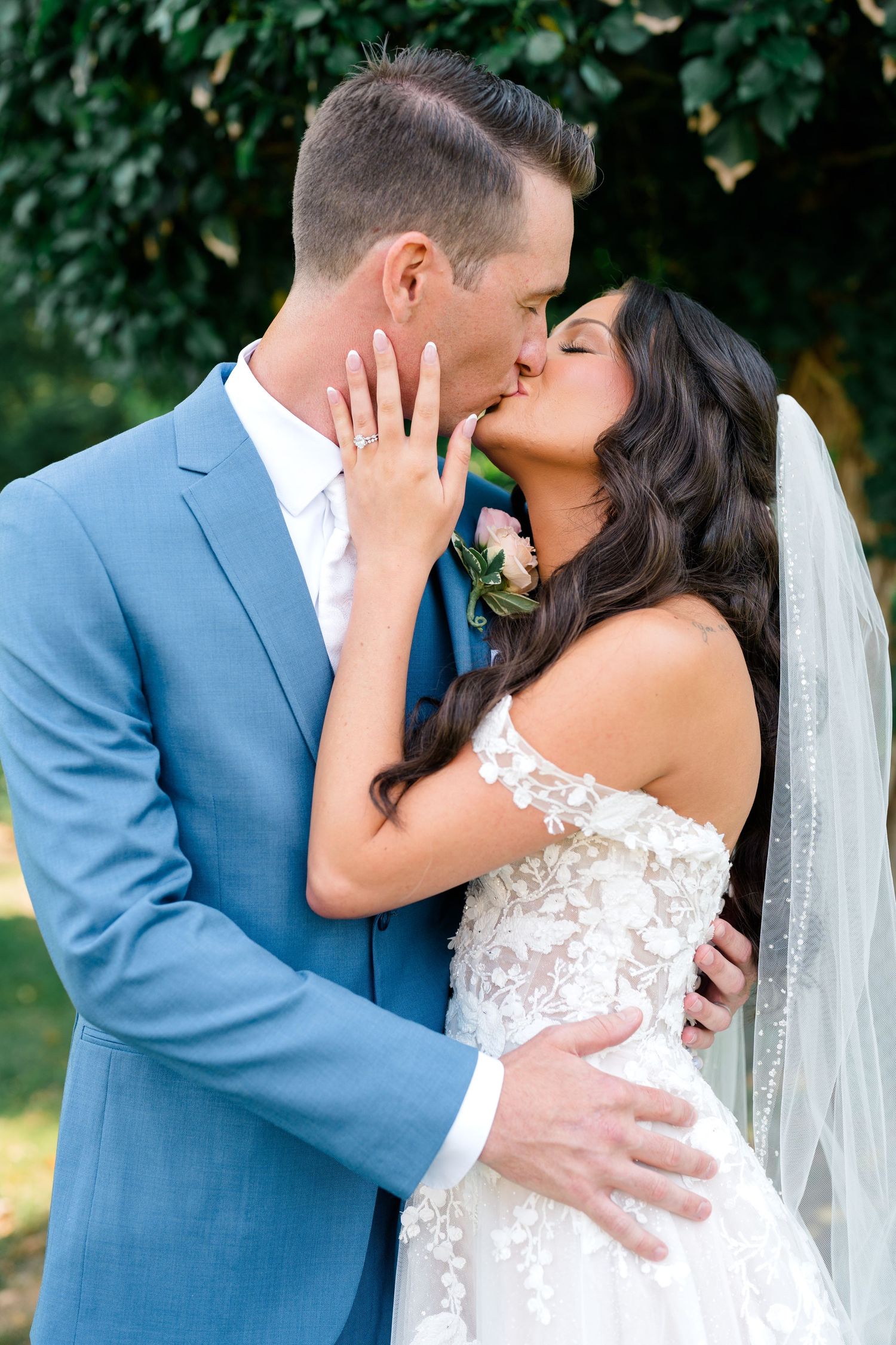 Romantic outdoor wedding portraits showing couple kissing in blue suit and white dress.