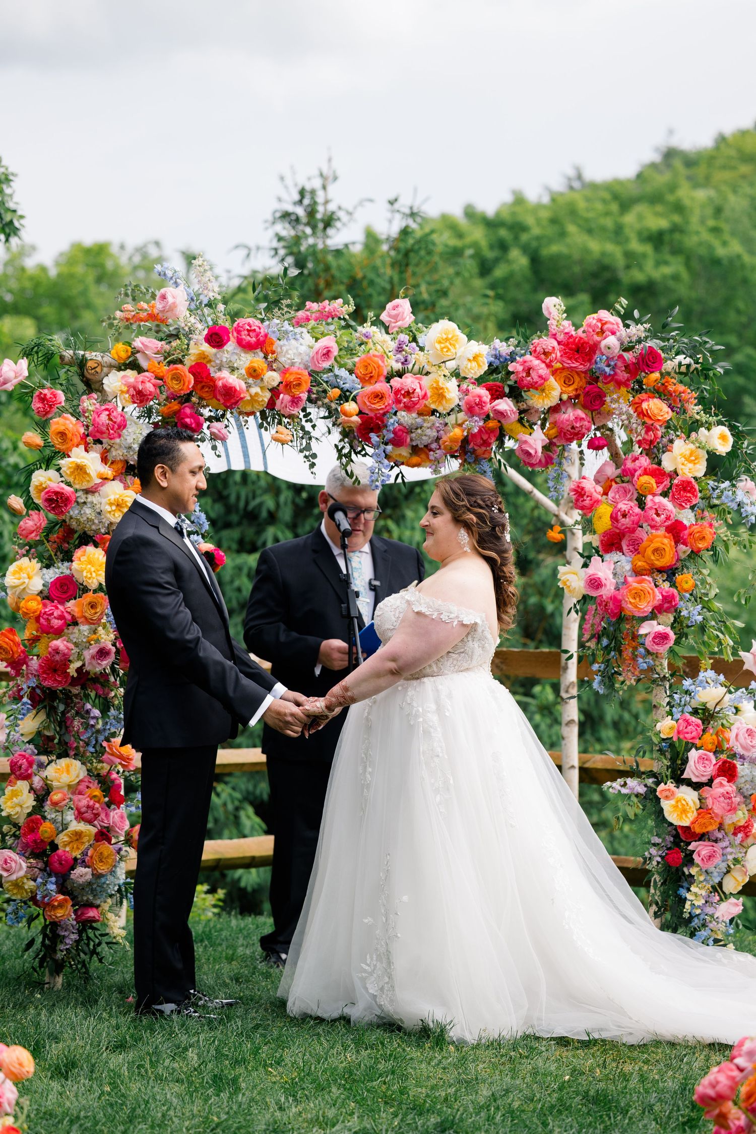 Wedding ceremony under spectacular floral arch with vibrant pink, orange and yellow blooms.