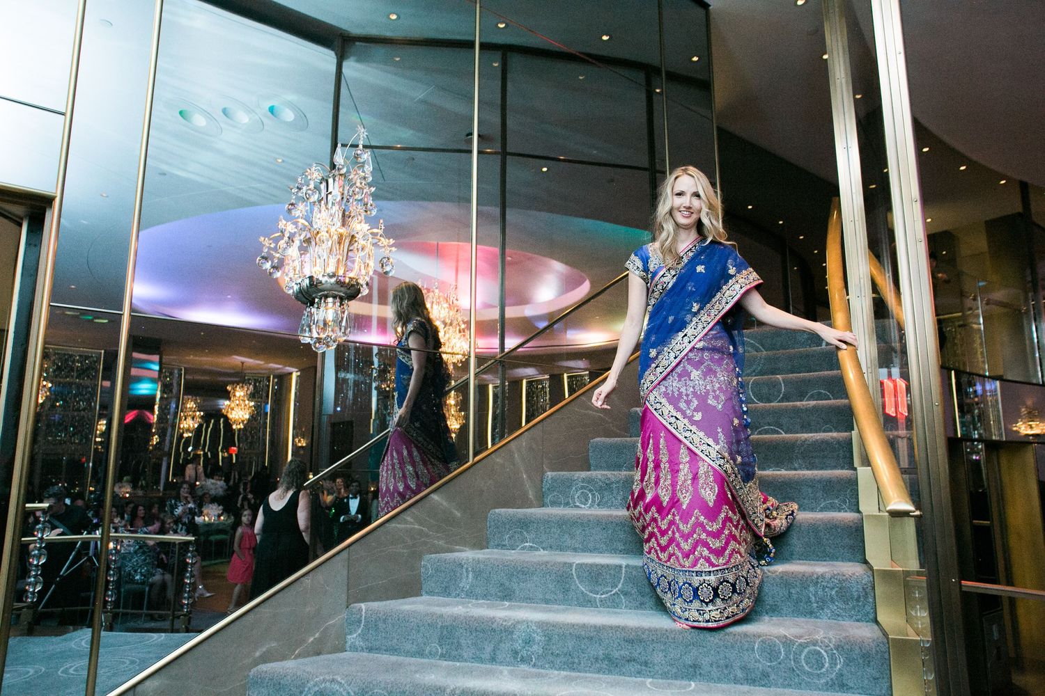 A person in a sparkly blue dress poses dramatically on an elegant staircase.