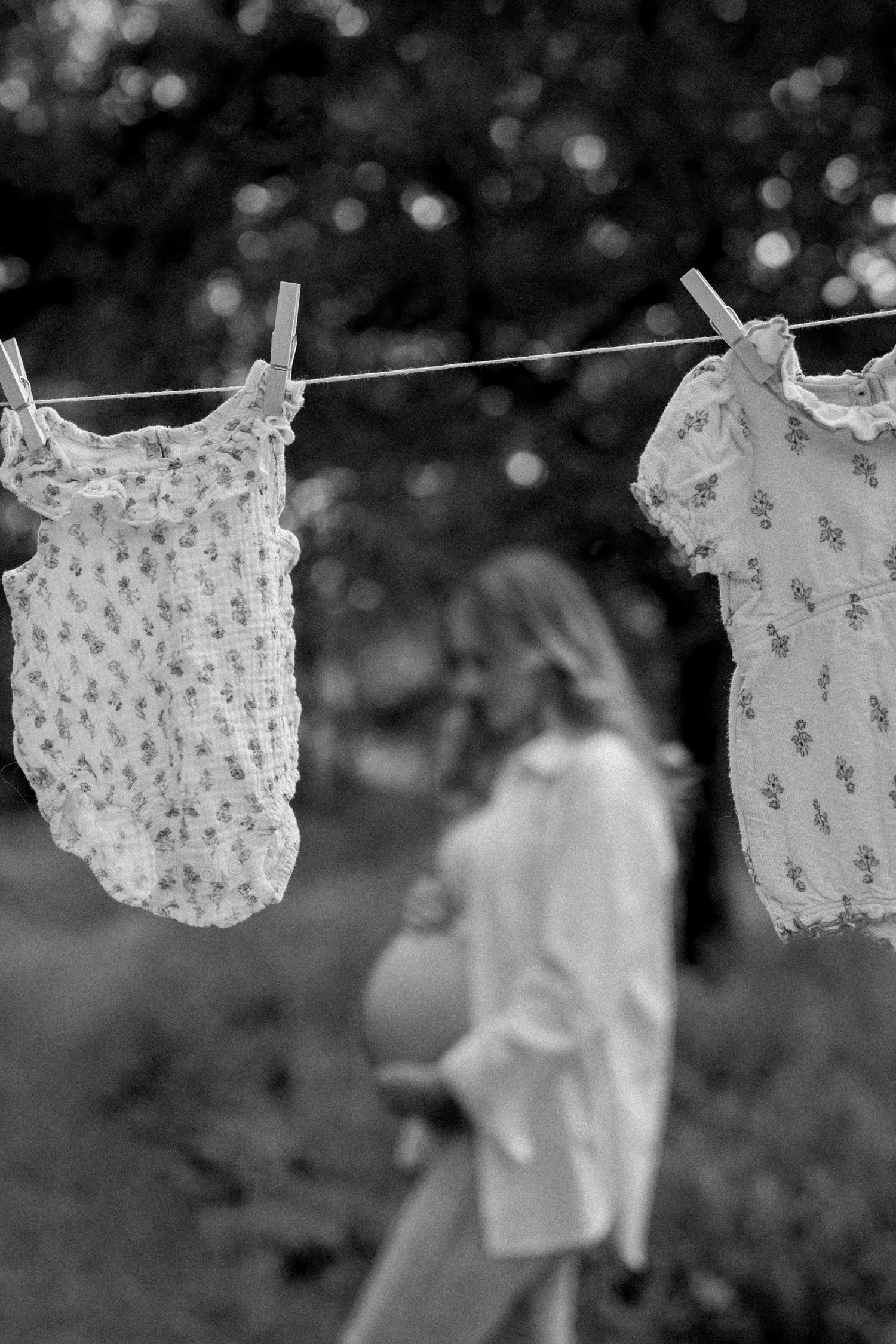 Baby onesies and clothing items hanging to dry on a clothesline outdoors in black and white.