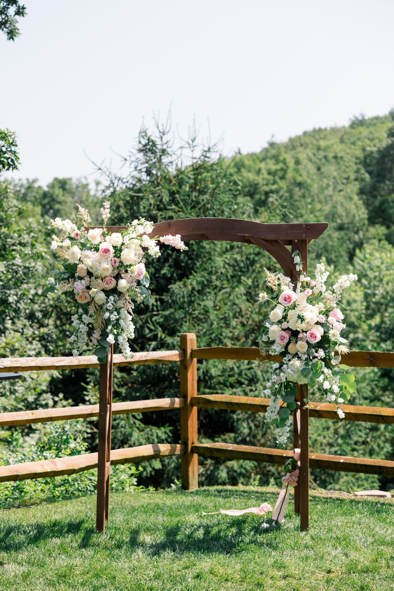 Rustic wooden split-rail fence decorated with pink and white floral arrangements.