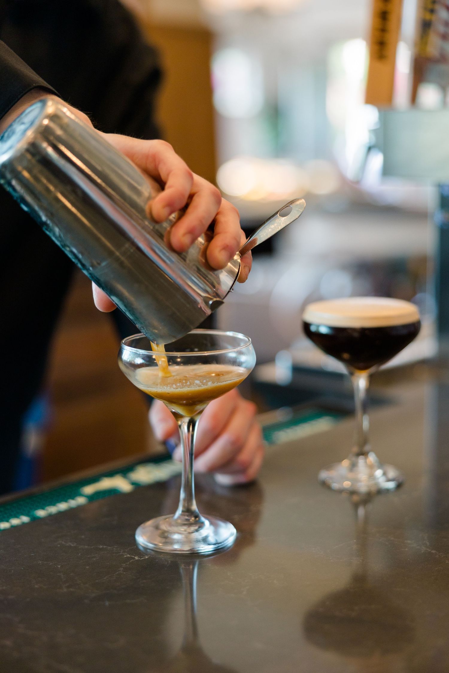 Bartender pouring an espresso martini from a shaker into a coupe glass at a wedding bar.