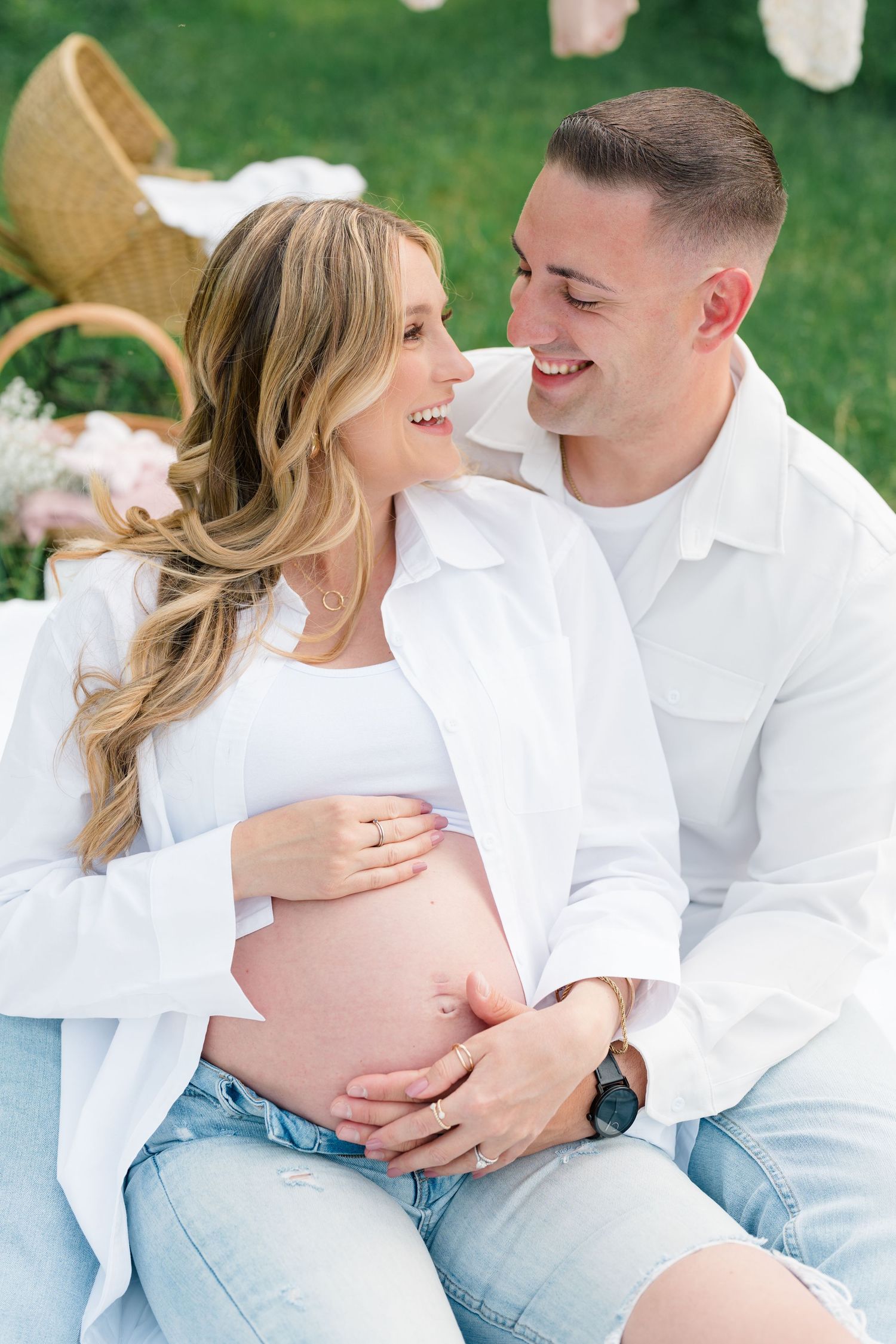 Intimate maternity photo with baby clothes hanging in background and wicker chair setting.
