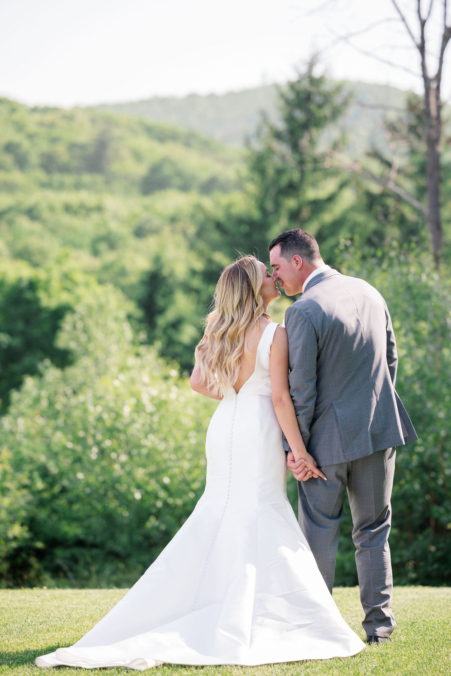 Newlyweds share a romantic moment on a hilltop surrounded by lush green scenery.