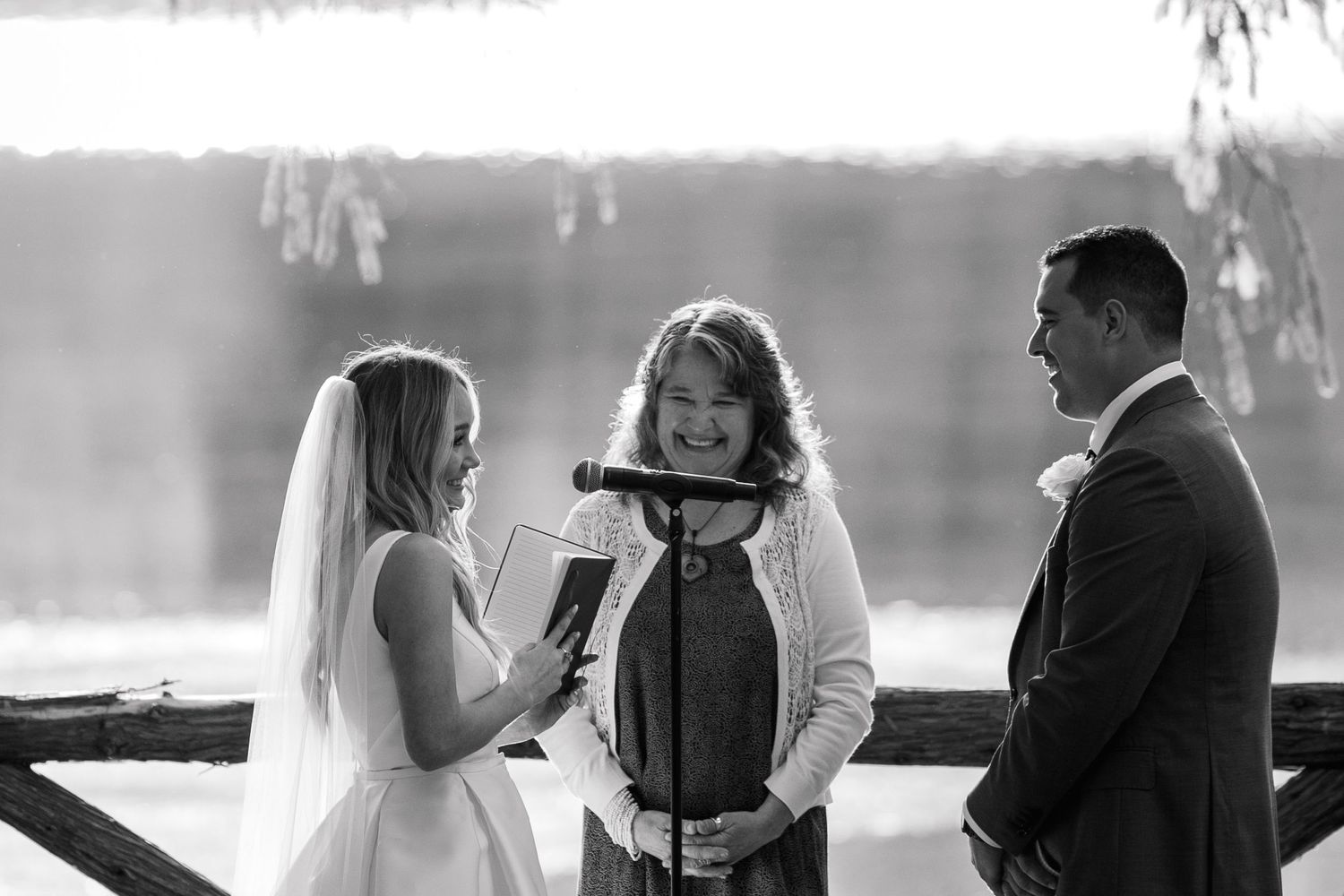 Outdoor wedding ceremony taking place on a wooden deck surrounded by pine trees.
