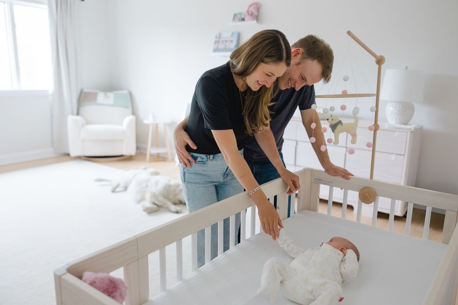 Parents bonding with their newborn baby on a white bed in a naturally lit room.