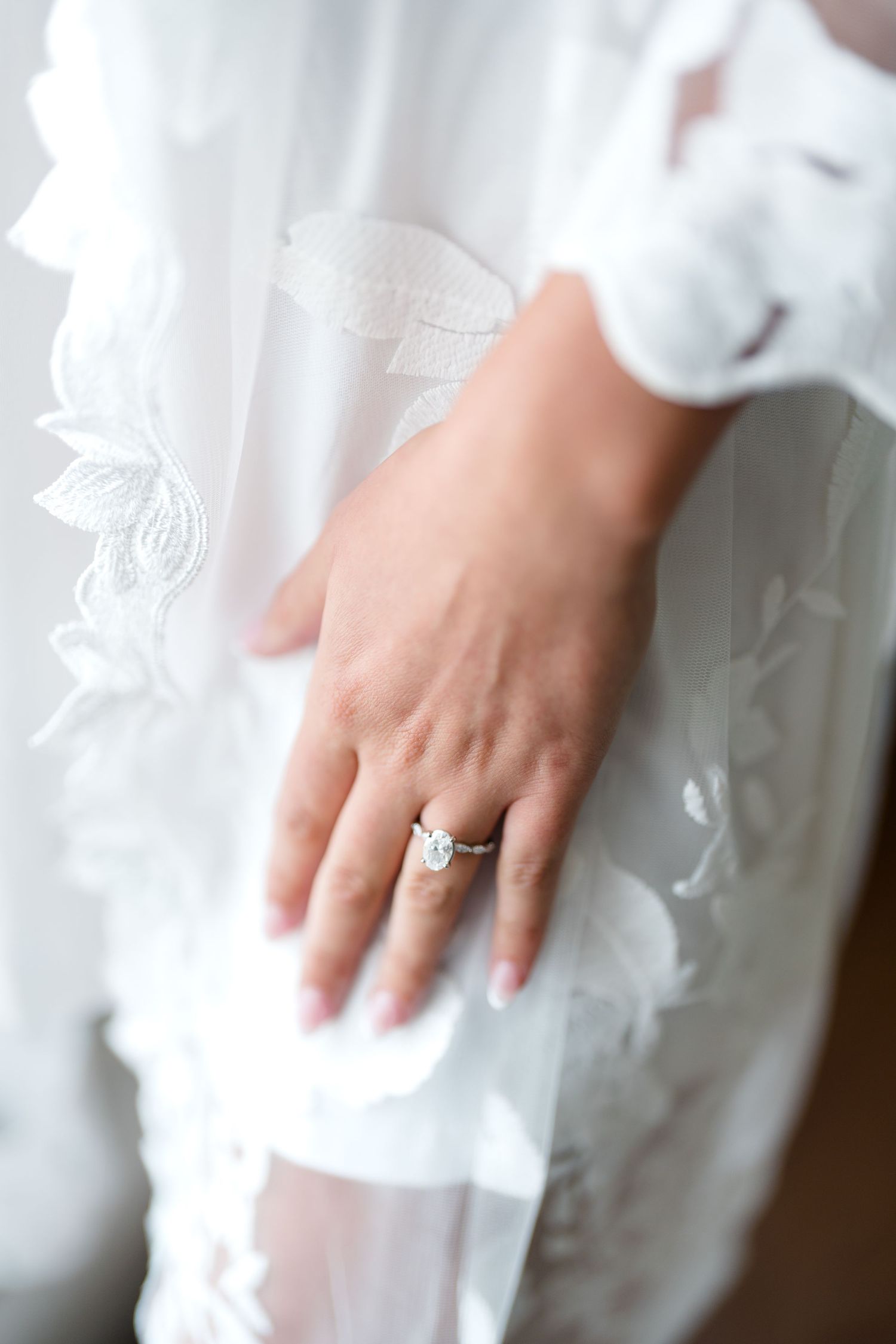 Close up of a delicate engagement ring on a hand against flowing white fabric.
