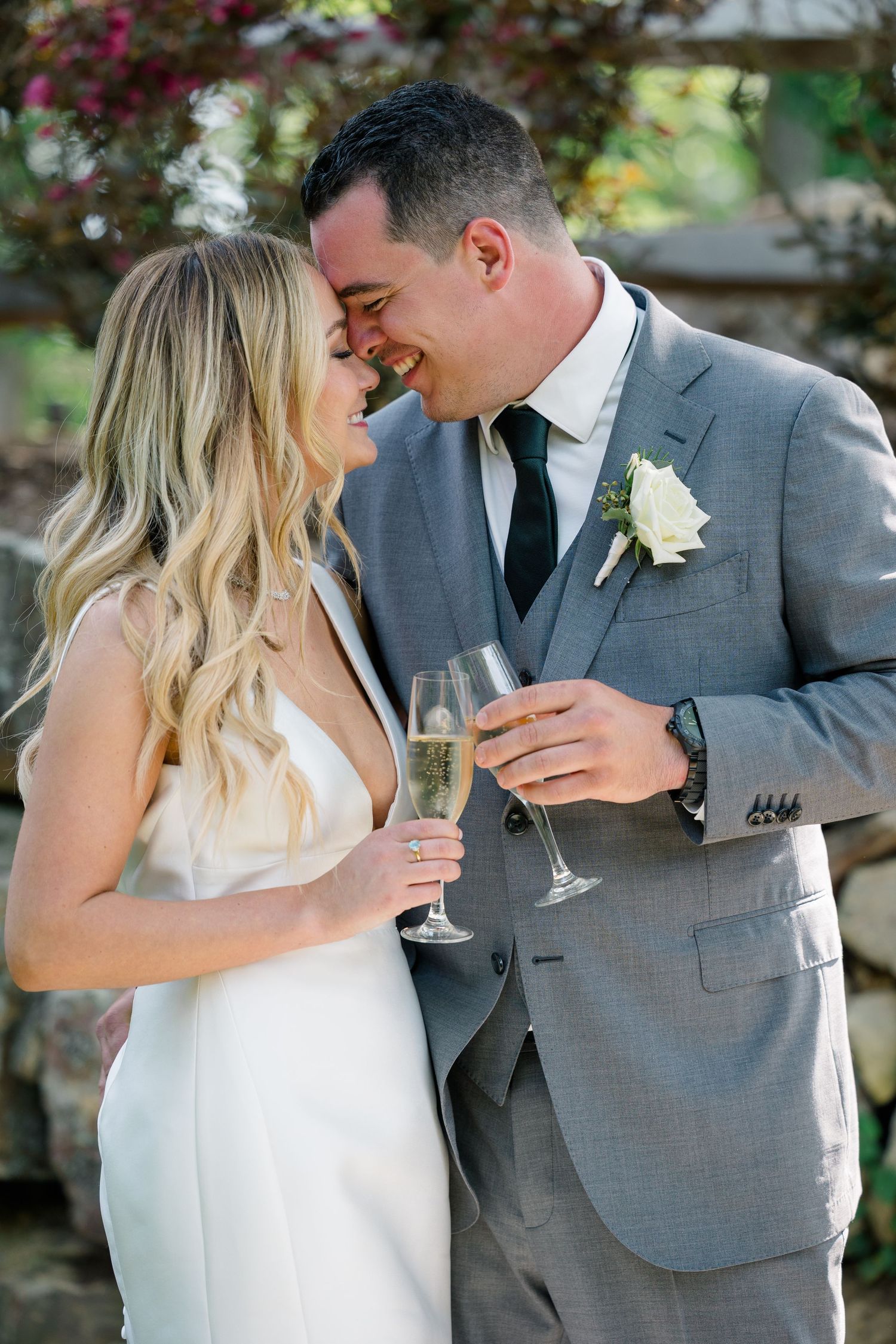A bride and groom share an intimate moment while holding champagne glasses in an outdoor garden setting.