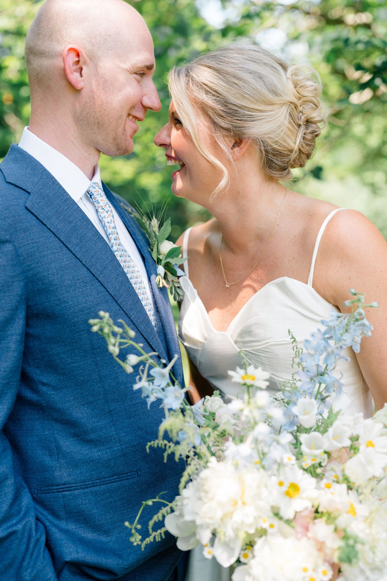 A smiling bride and groom share a joyful moment surrounded by a white and blue bouquet.