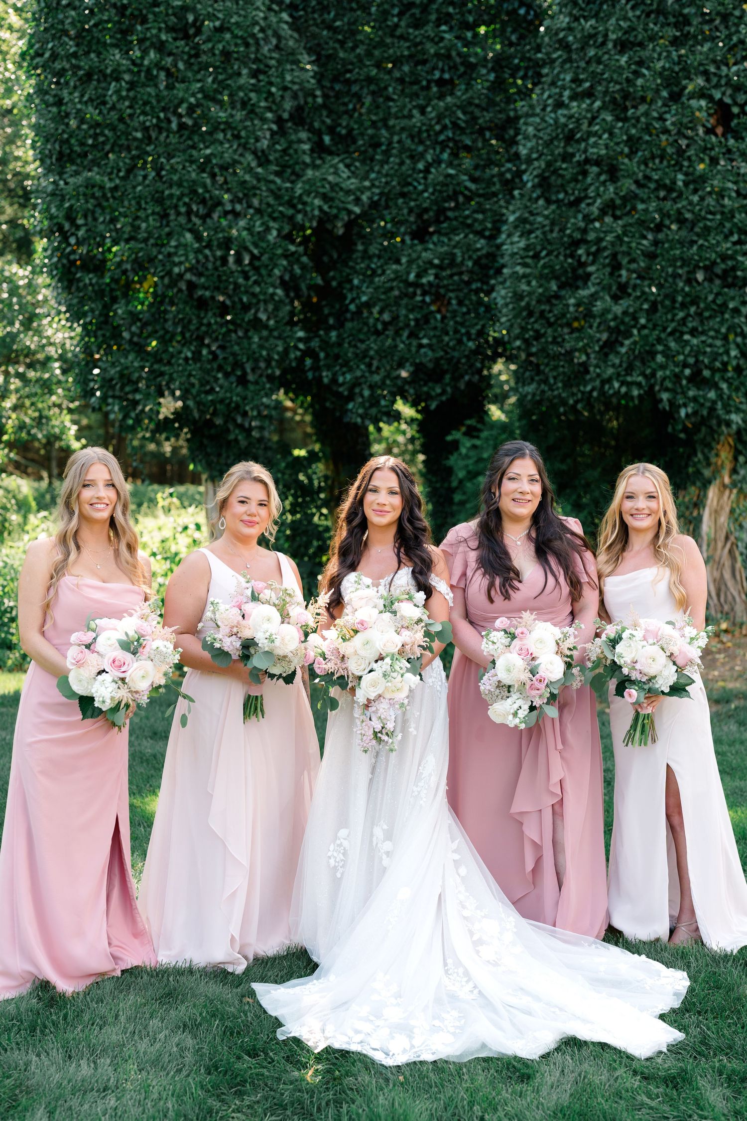 Bridal party in flowing pink and mauve dresses holding blush and white bouquets.