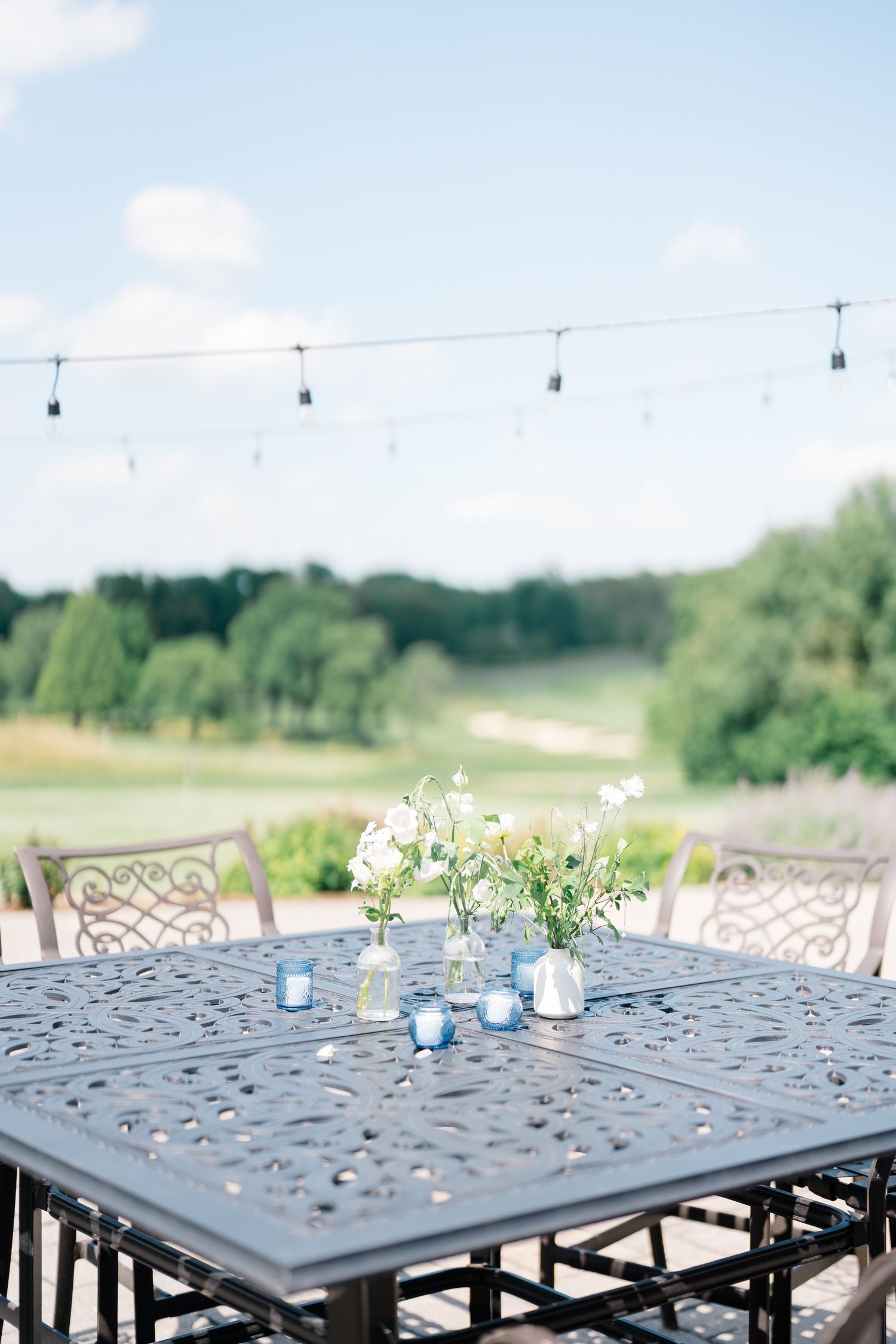 Elegant outdoor patio table with white floral centerpiece and blue votives overlooking a golf course.