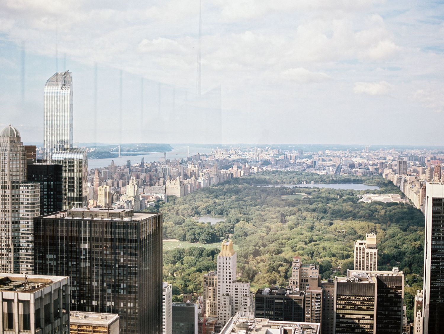 Aerial view of Central Park and Manhattan skyline with modern skyscrapers against a blue sky.