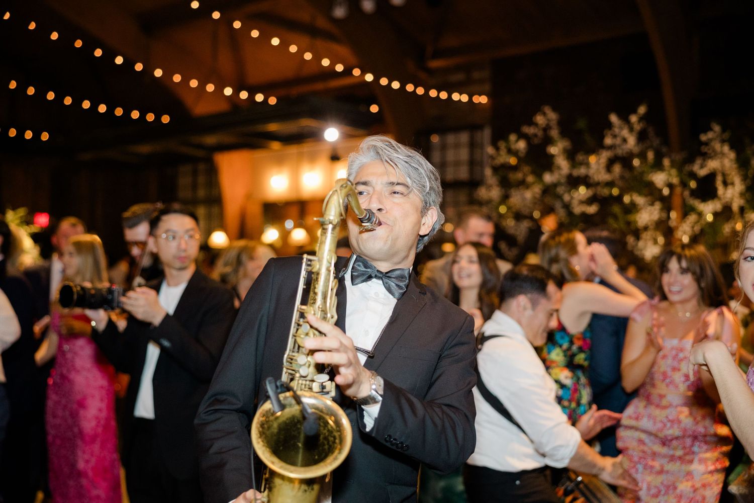 Saxophone player performs at elegant wedding reception under crystal chandeliers.