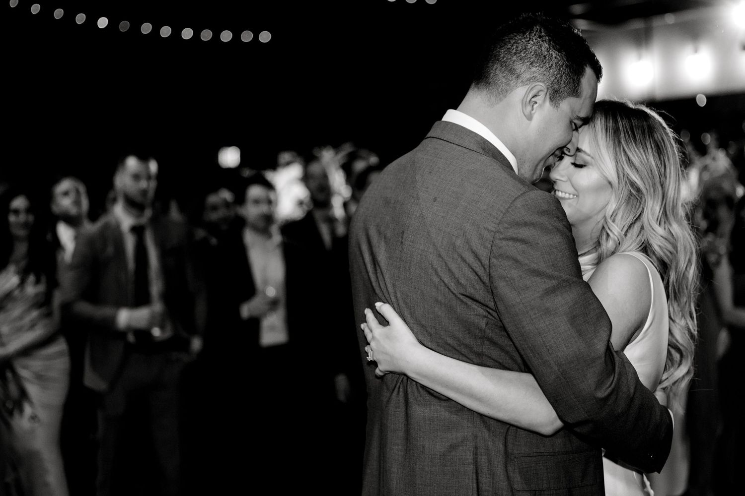 Couple sharing an intimate dance moment under string lights at their wedding reception.