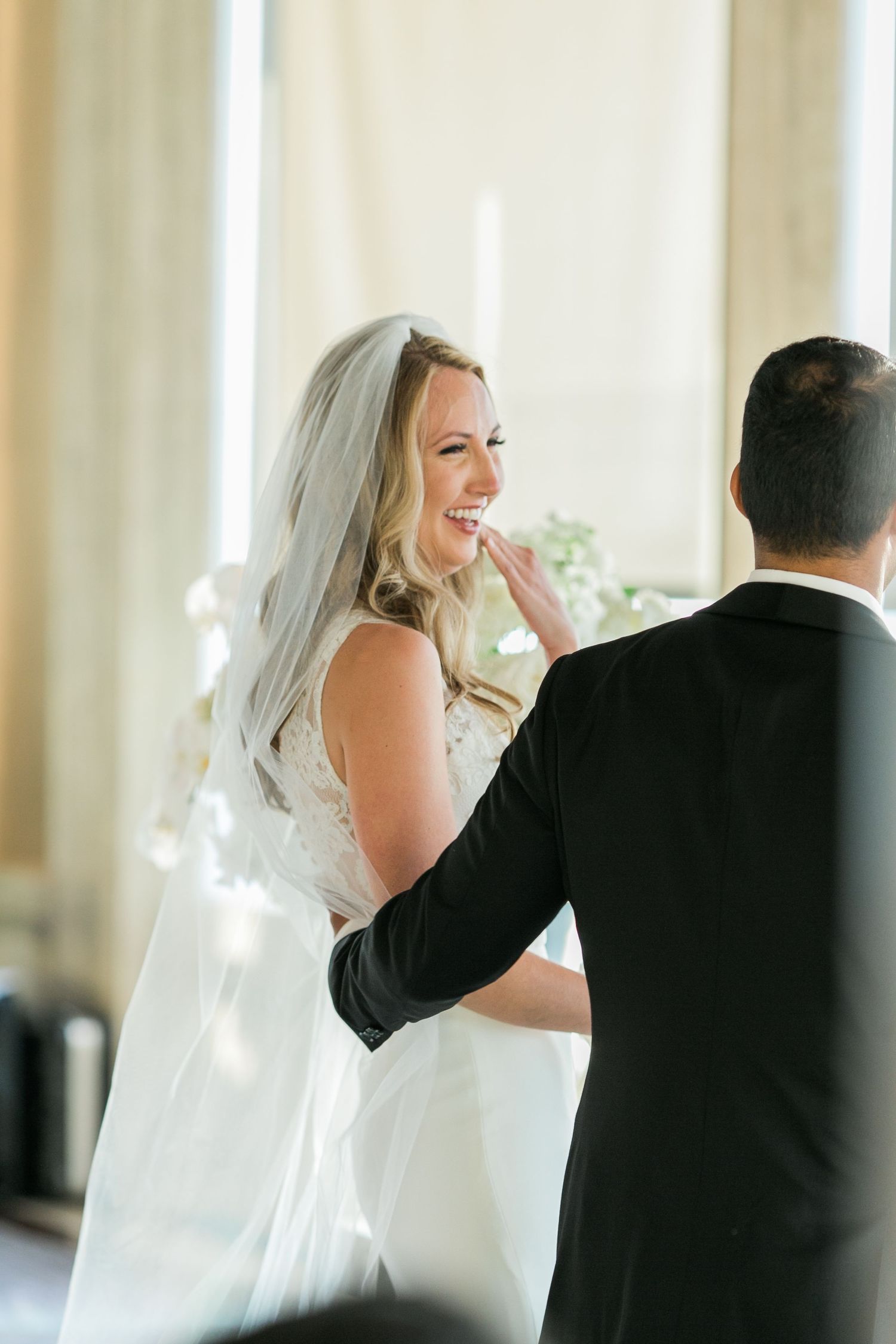 A joyful bride in a white dress and veil glances over her shoulder while dancing with her groom during their wedding.