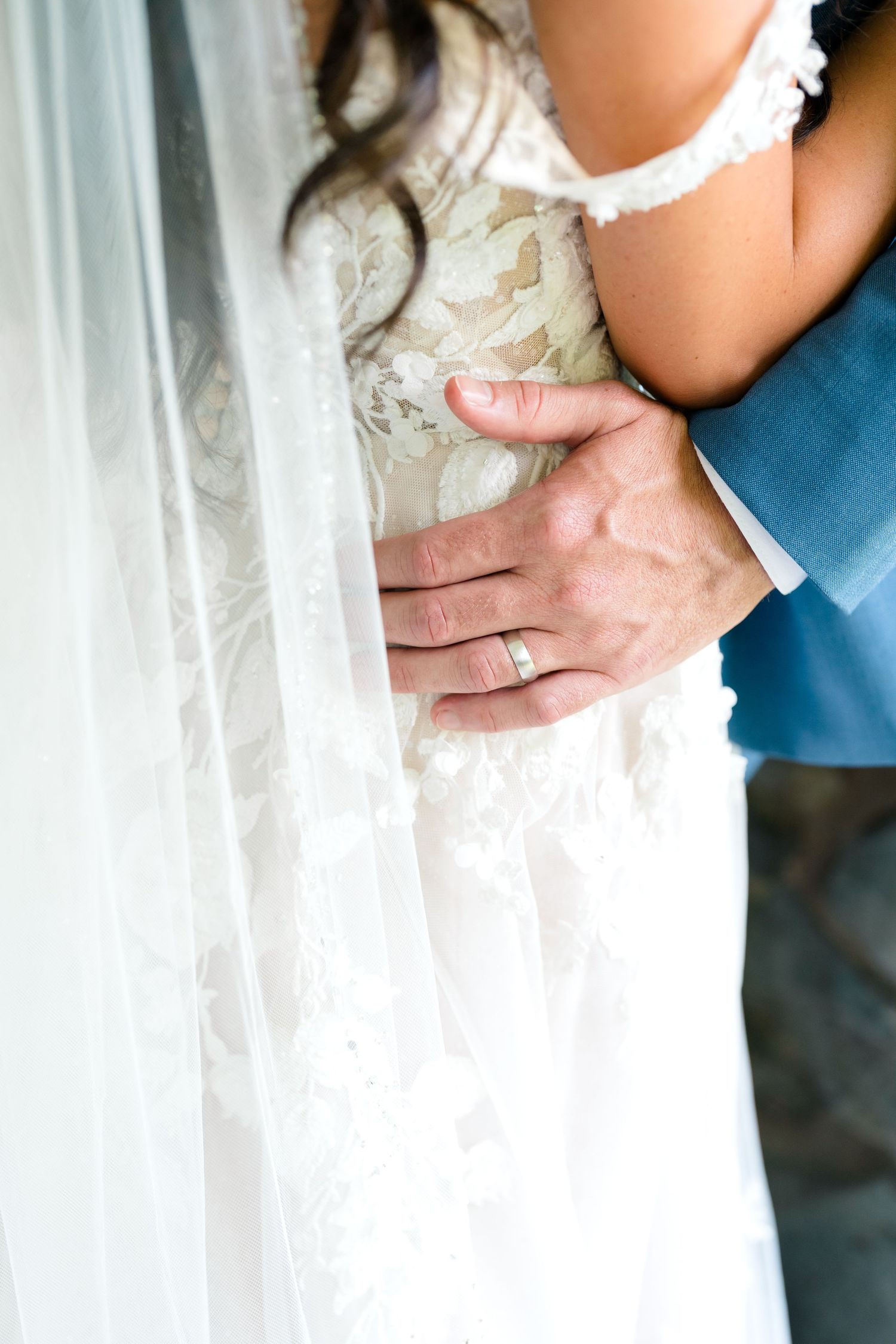 Detail shot of delicate lace on a flowing white wedding dress against a light background.
