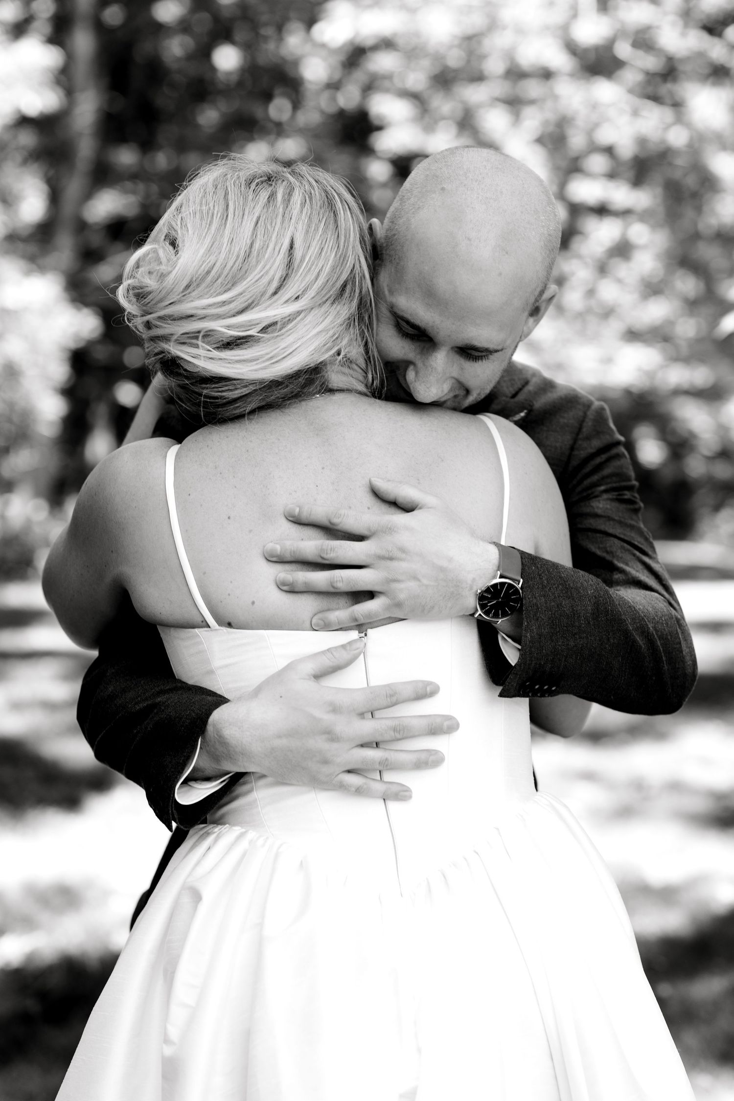 Emotional black and white photo of bride and groom sharing a tender embrace outdoors on their wedding day.