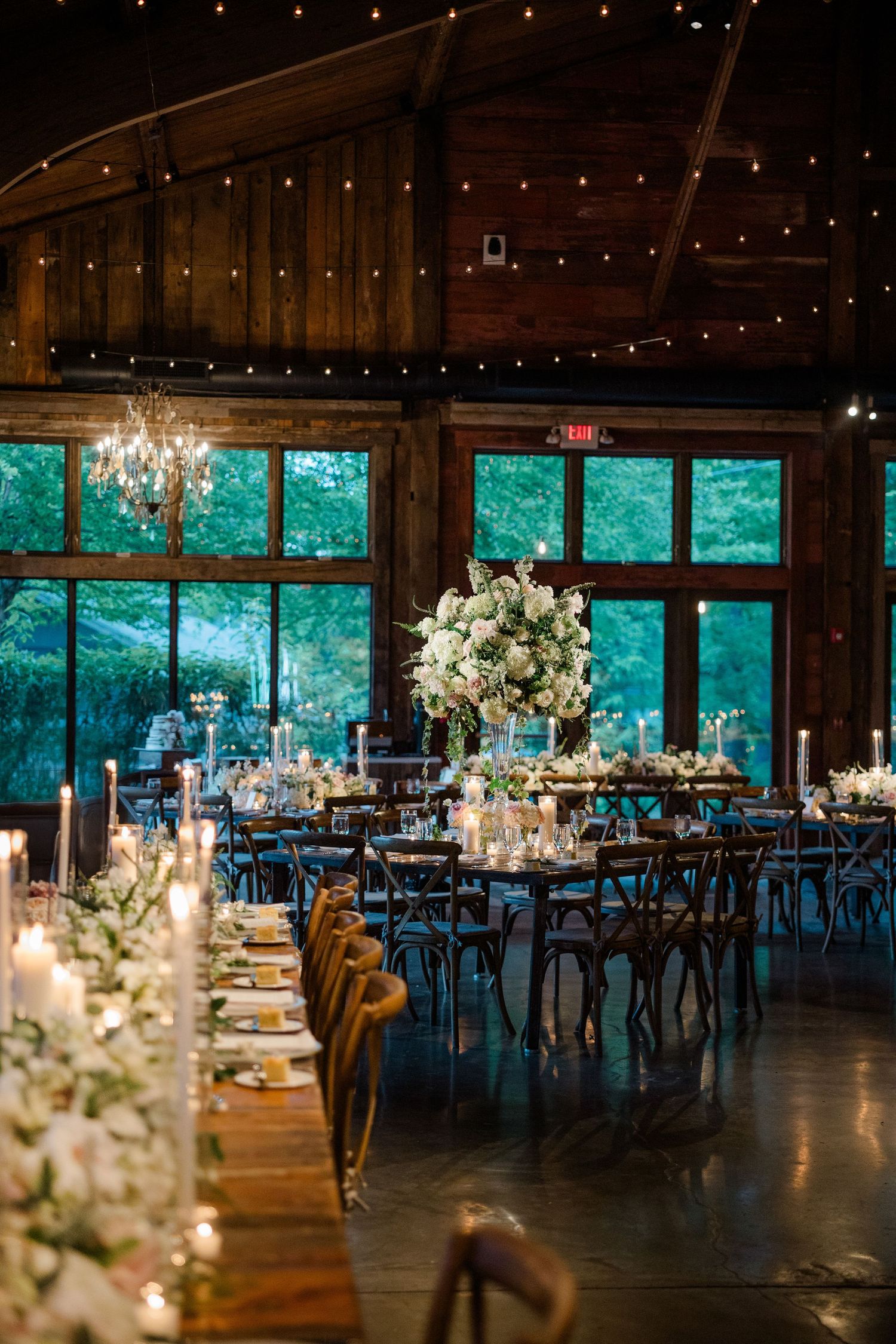 Elegant rustic wedding reception venue with floor-to-ceiling windows and crystal chandeliers.