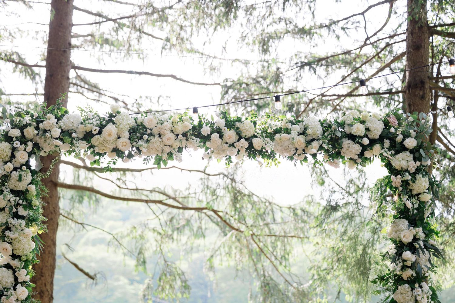 Elegant floral arch with white roses and greenery decorating an outdoor wedding space.
