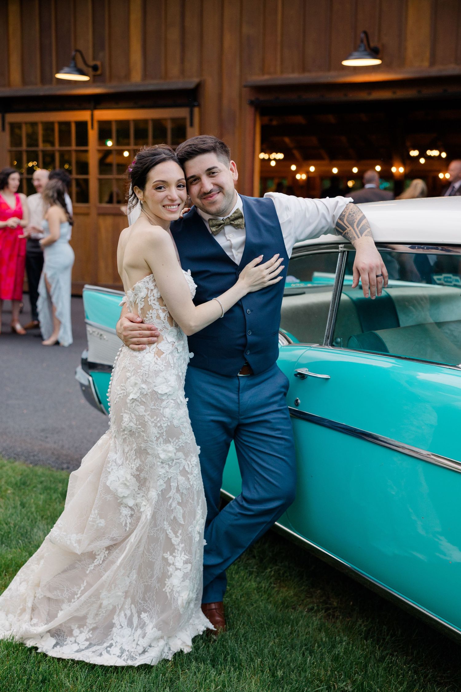 A couple poses beside a vintage turquoise car at their wedding reception.