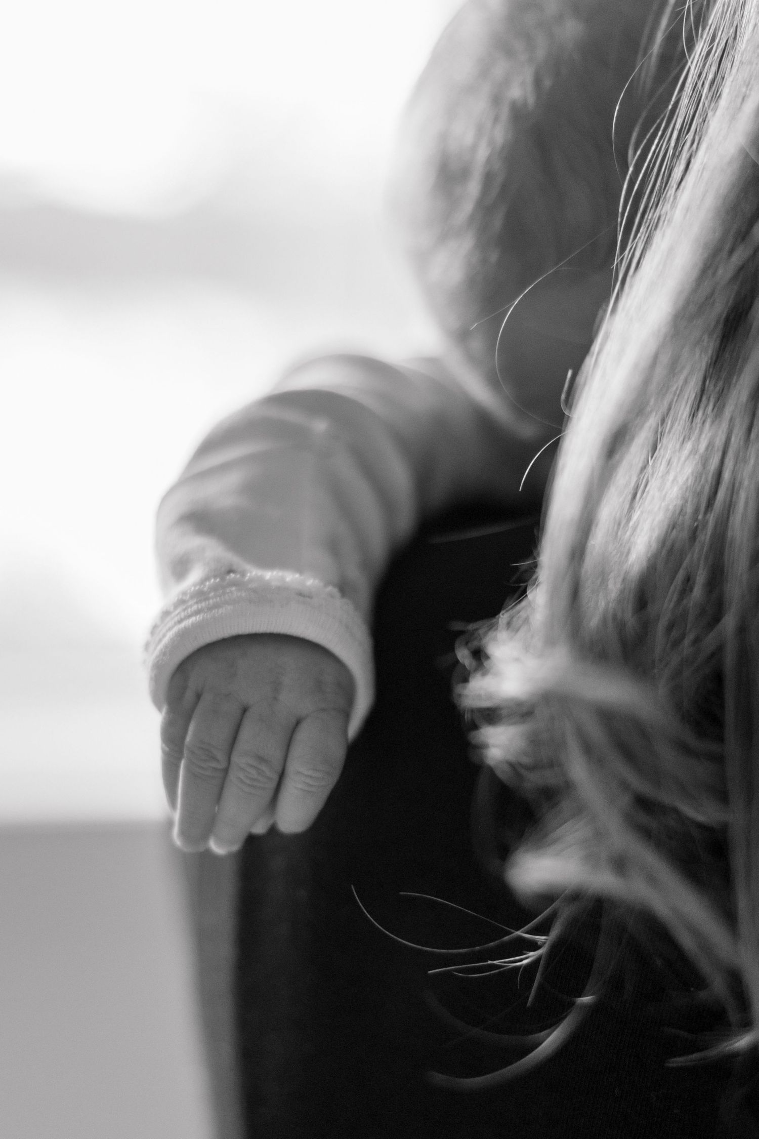 Close-up of a newborn baby's tiny hand reaching upward against a soft light background.