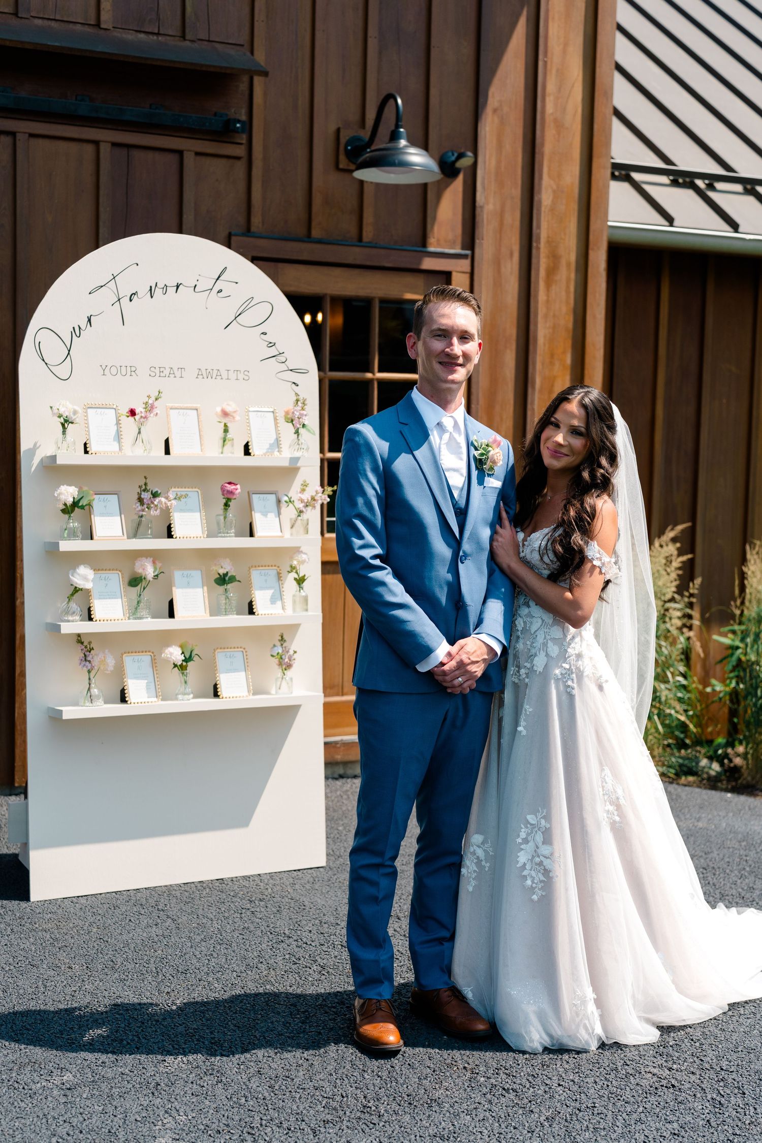 Wedding couple poses beside a rustic wooden wall with white display shelves at their reception venue.