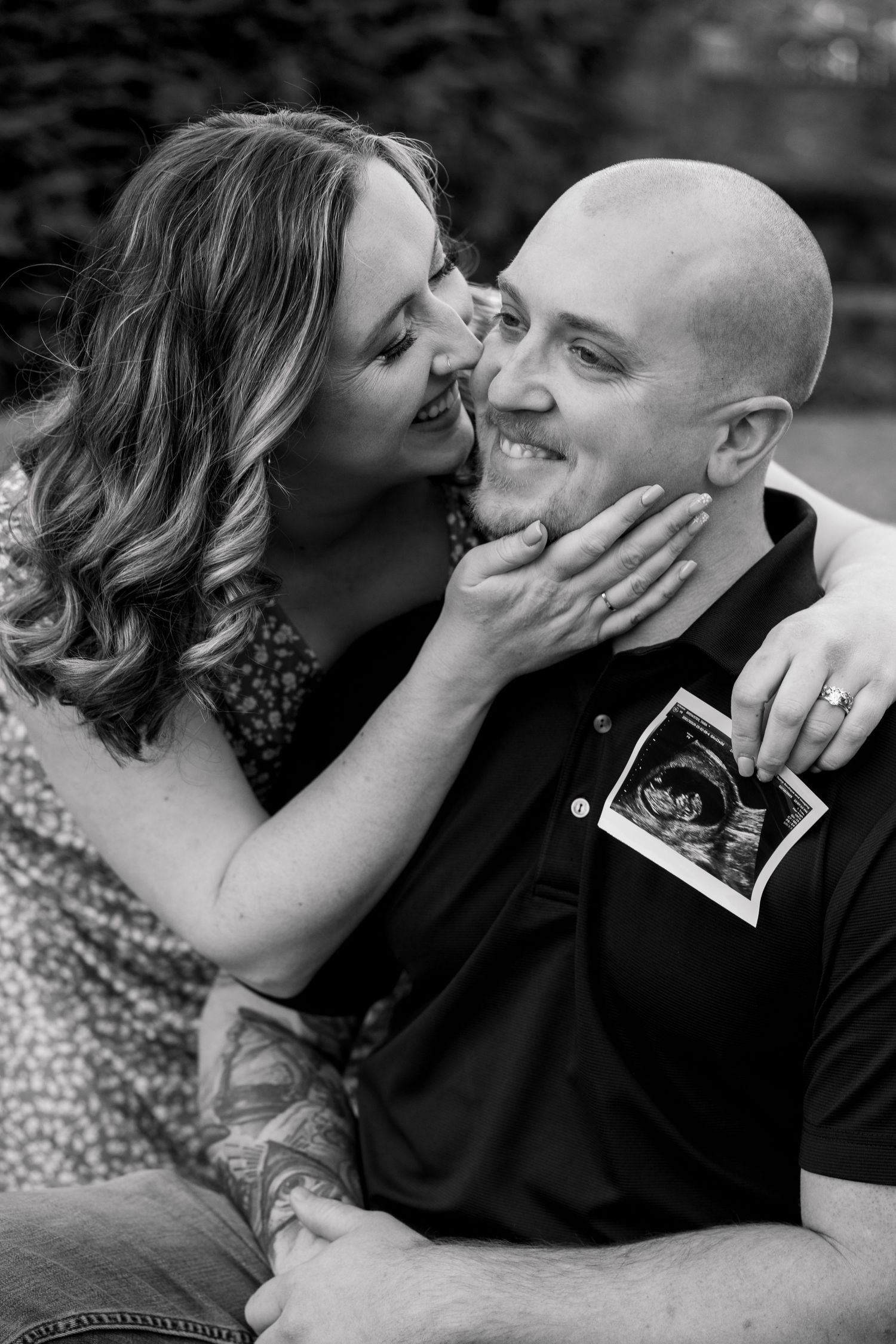 A couple shares an intimate black and white moment while holding an ultrasound photo during their pregnancy announcement.