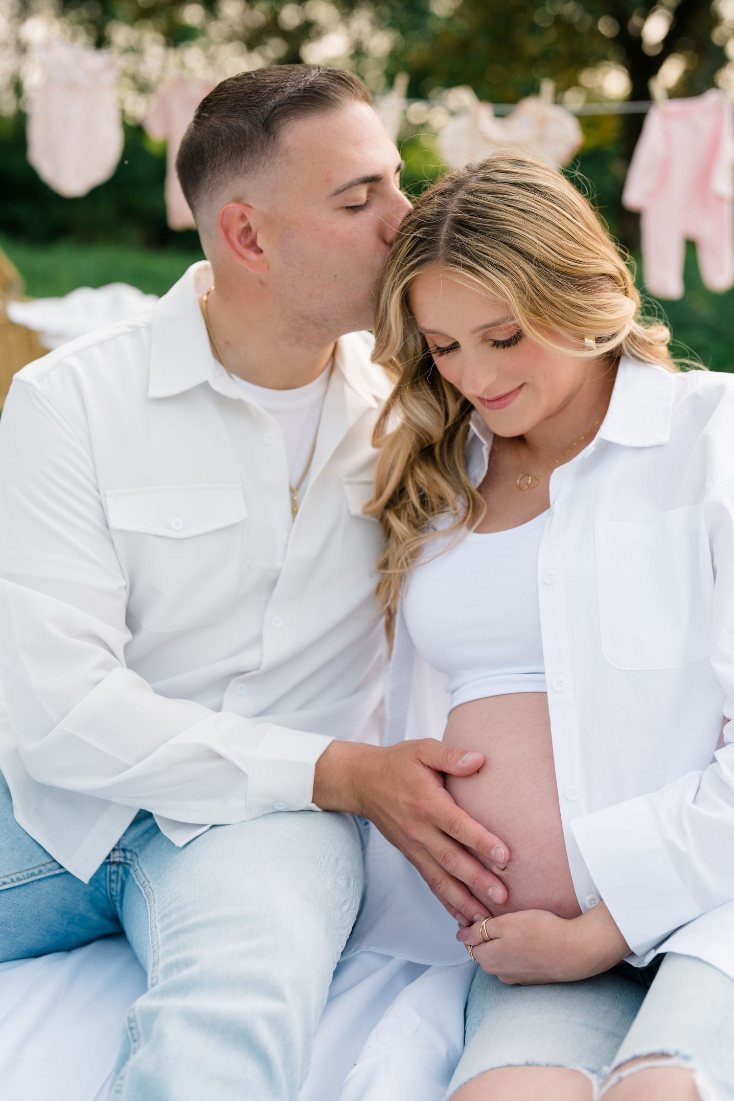 A maternity photoshoot in a garden setting with white clothing and baby clothes hanging on a clothesline in the background.
