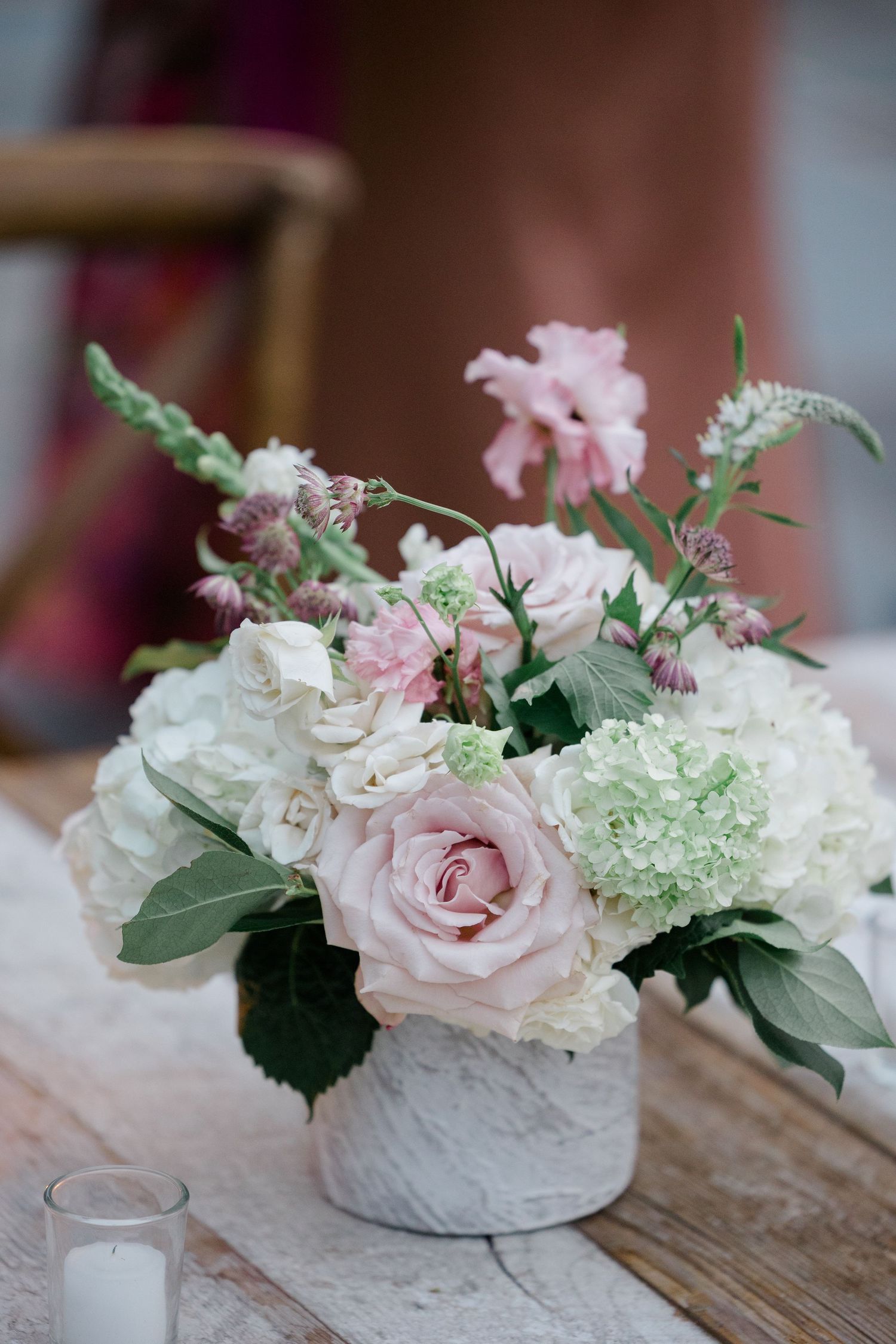 Delicate pink and white floral centerpiece with roses and hydrangeas in a textured vase.