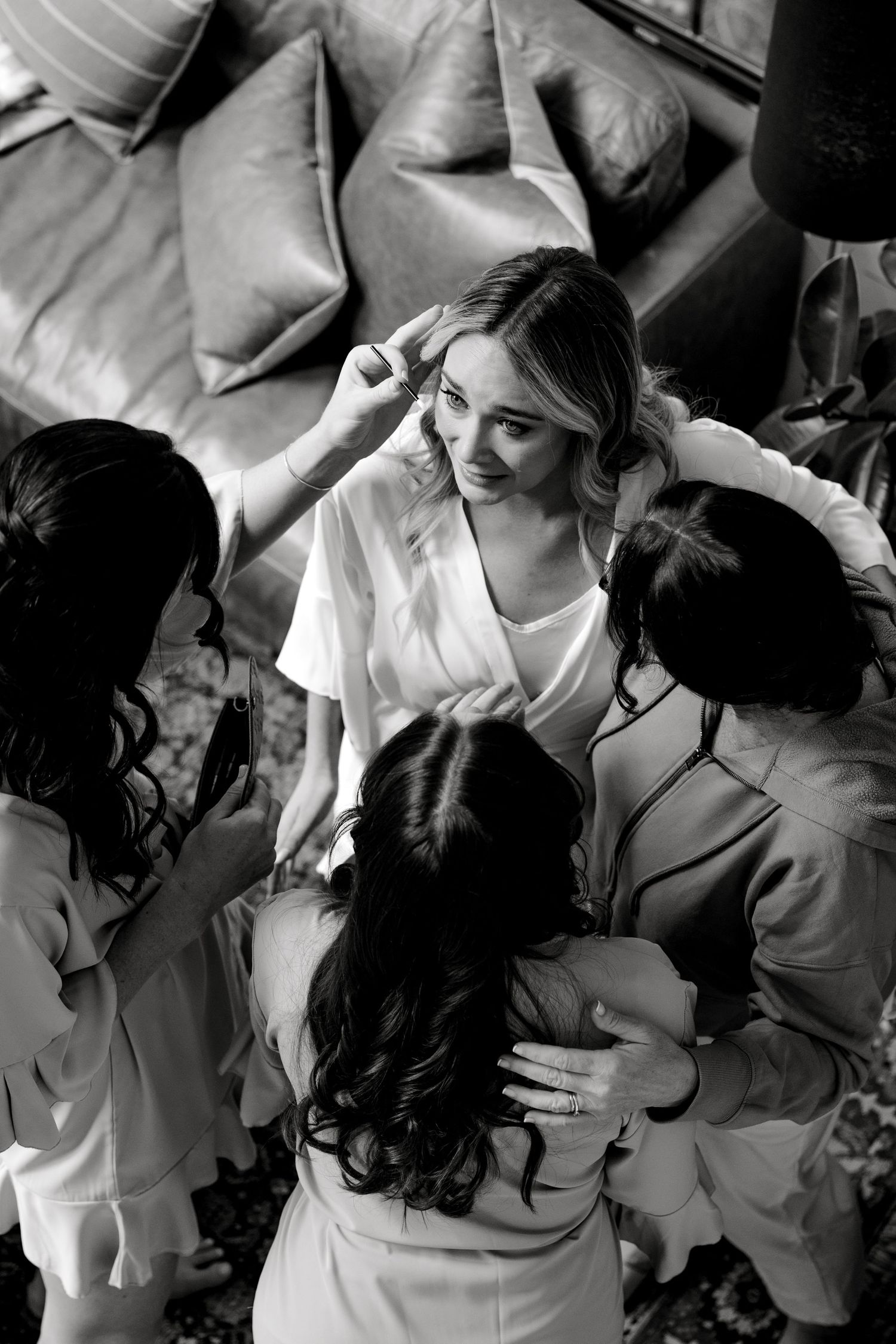 Black and white photo showing preparation moments with styling team working on bride's hair and makeup.