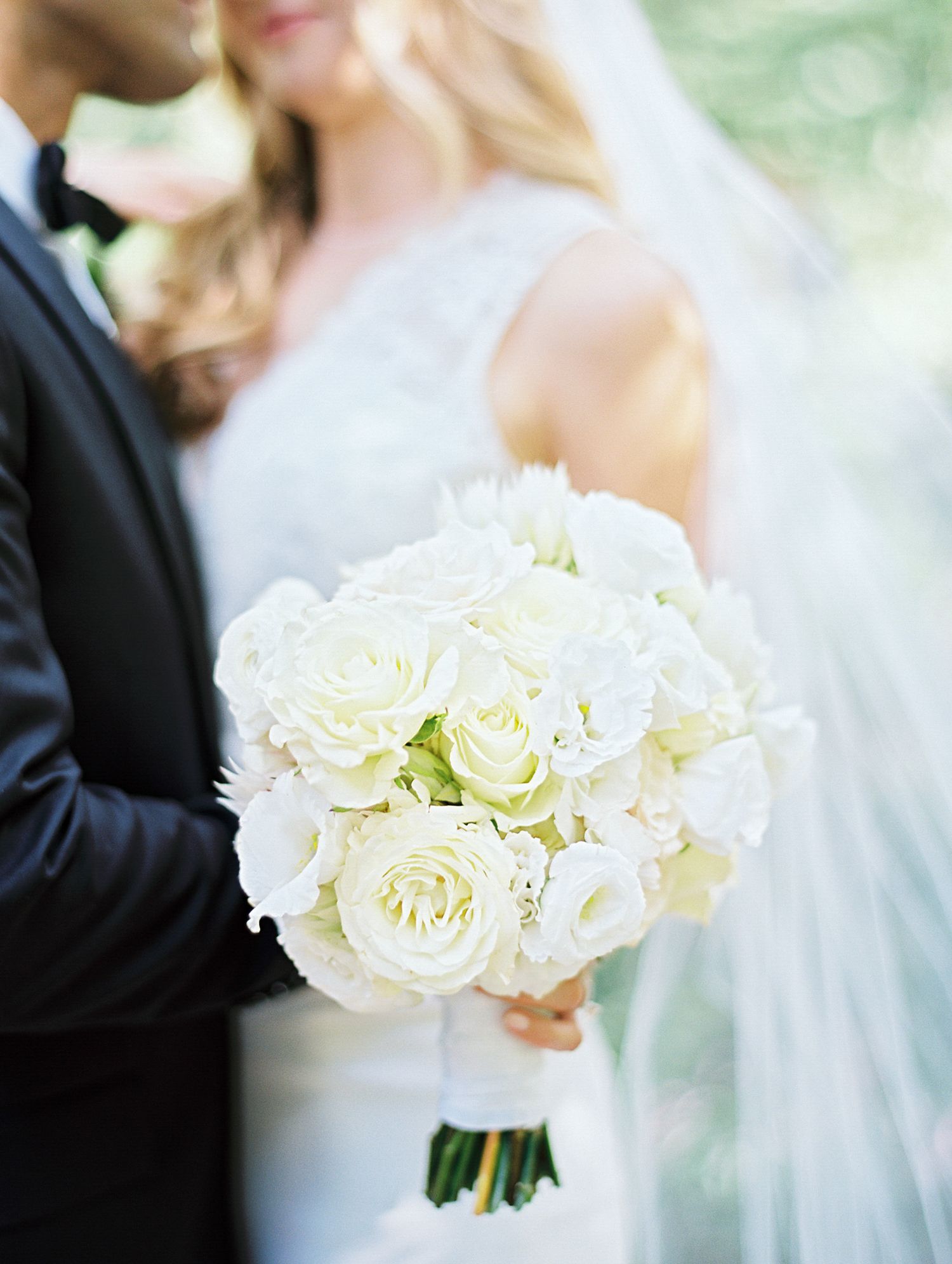 A classic white rose and hydrangea bridal bouquet shown against a formal wedding attire background.