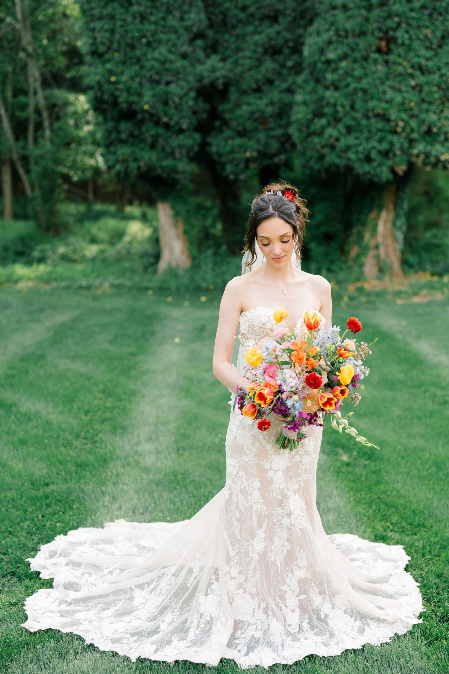 Bride in lace wedding gown holds vibrant wildflower bouquet in garden setting.