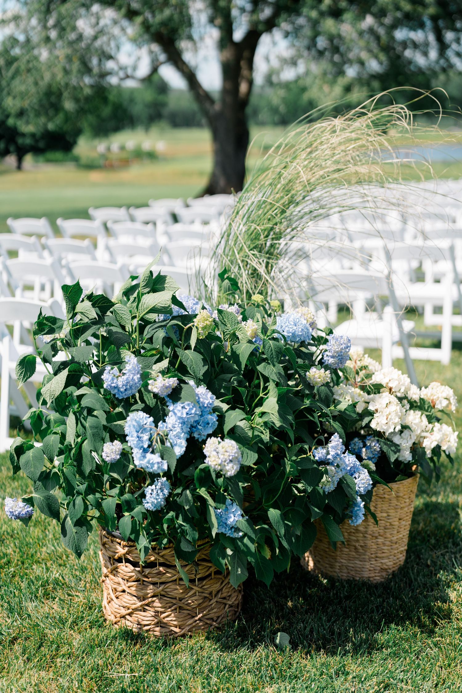 Wicker baskets filled with blue and white hydrangeas decorate outdoor wedding ceremony with white chairs.