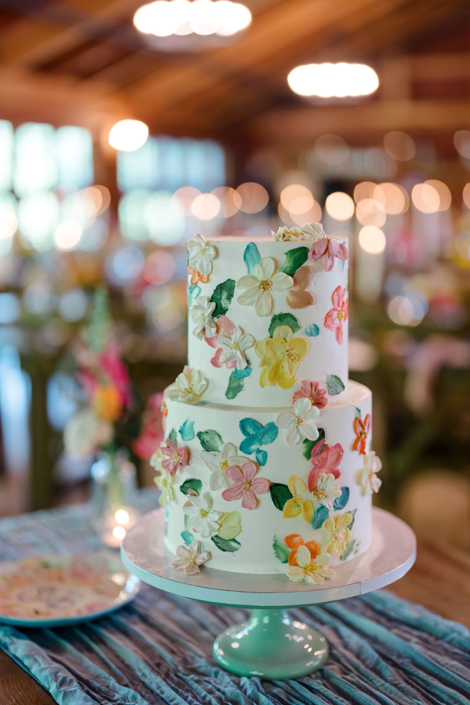 Two-tiered white wedding cake decorated with watercolor floral design on mint green cake stand.