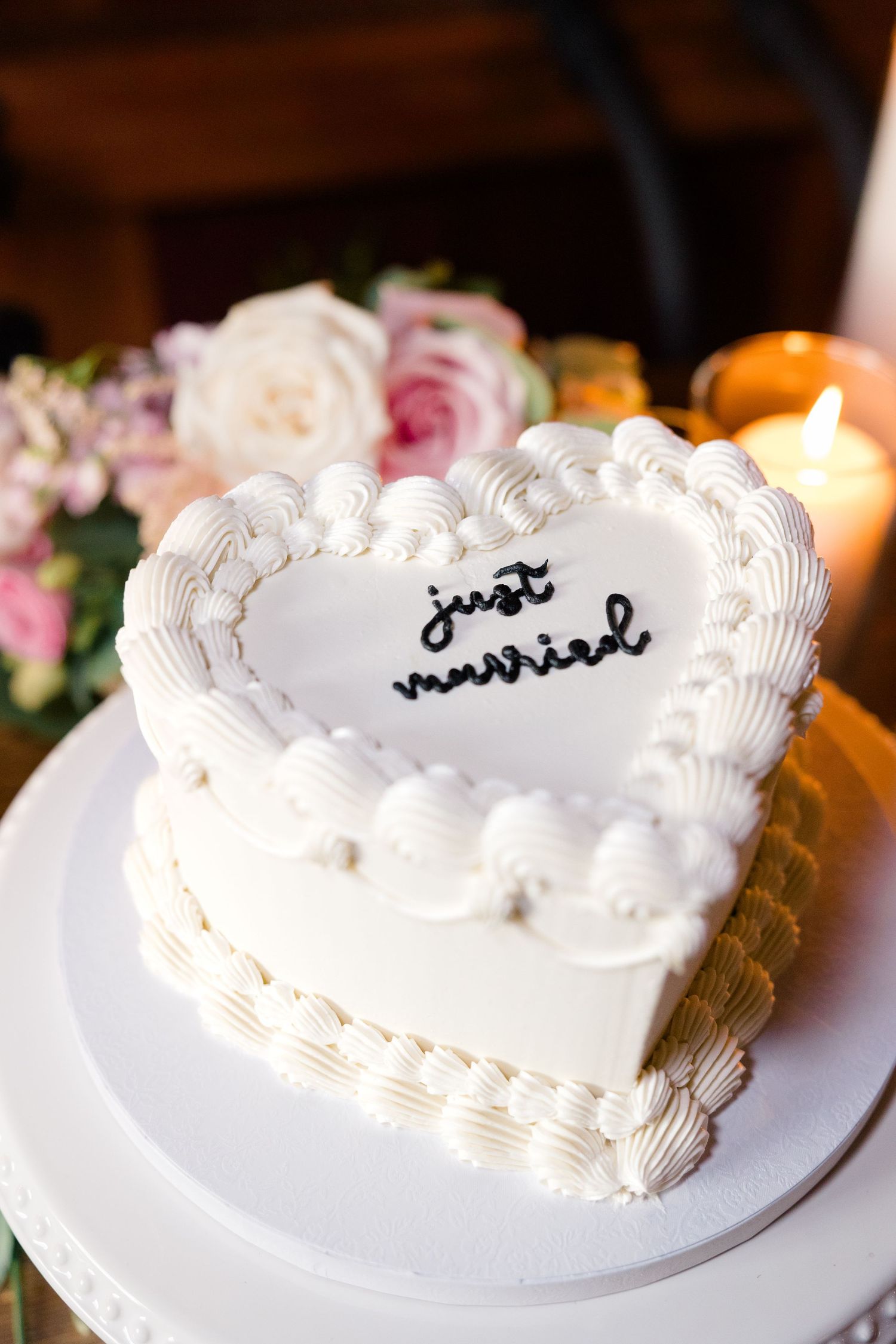 Heart-shaped white wedding cake with delicate piped frosting details on display at reception.