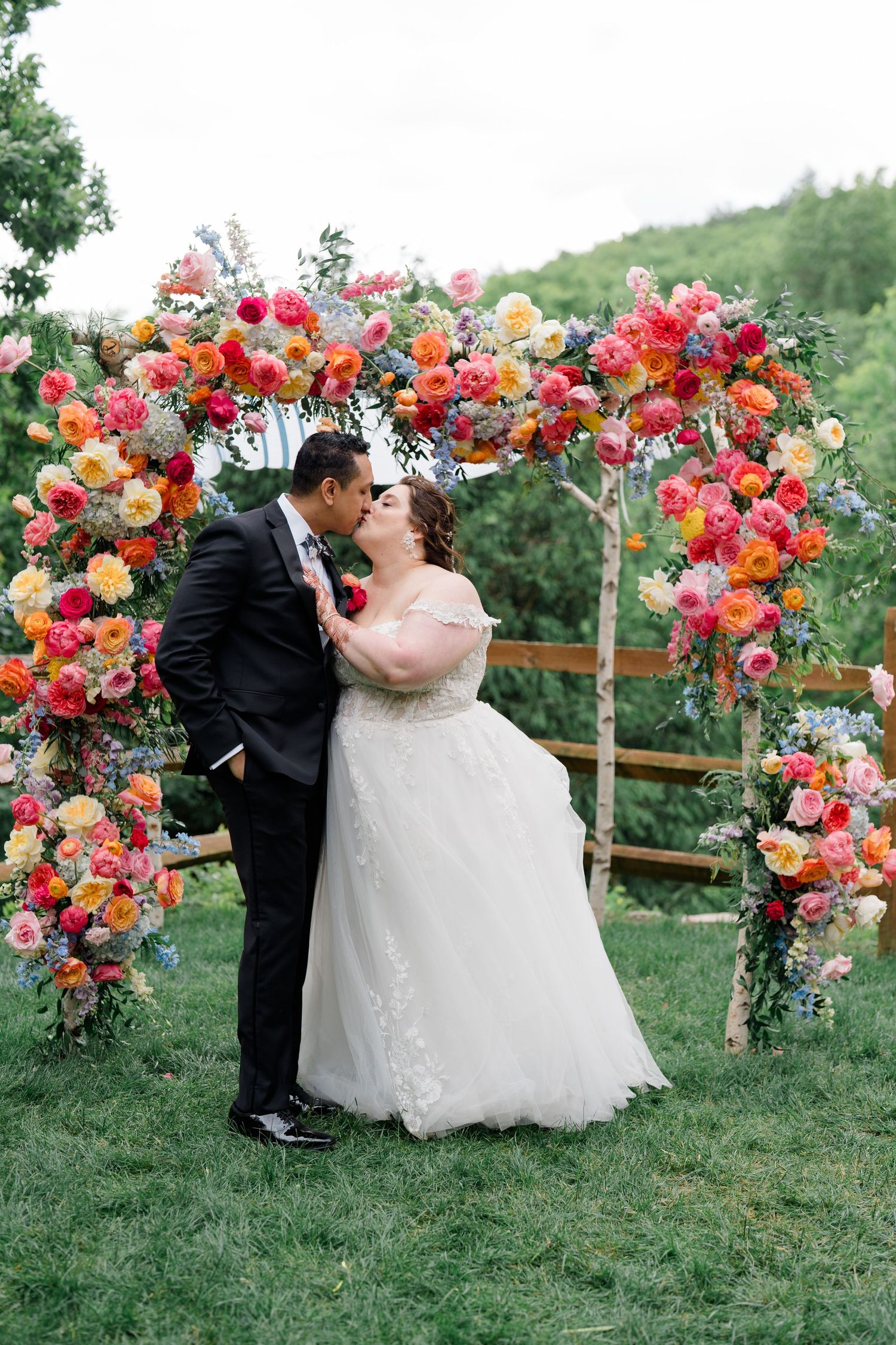 Romantic wedding moment under magnificent floral arch with pink, orange and red roses.