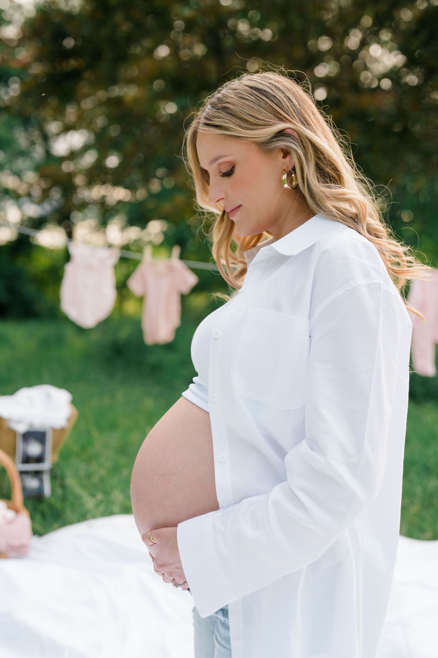 Maternity portrait outdoors with white button-down shirt and baby clothes hanging on clothesline in background.