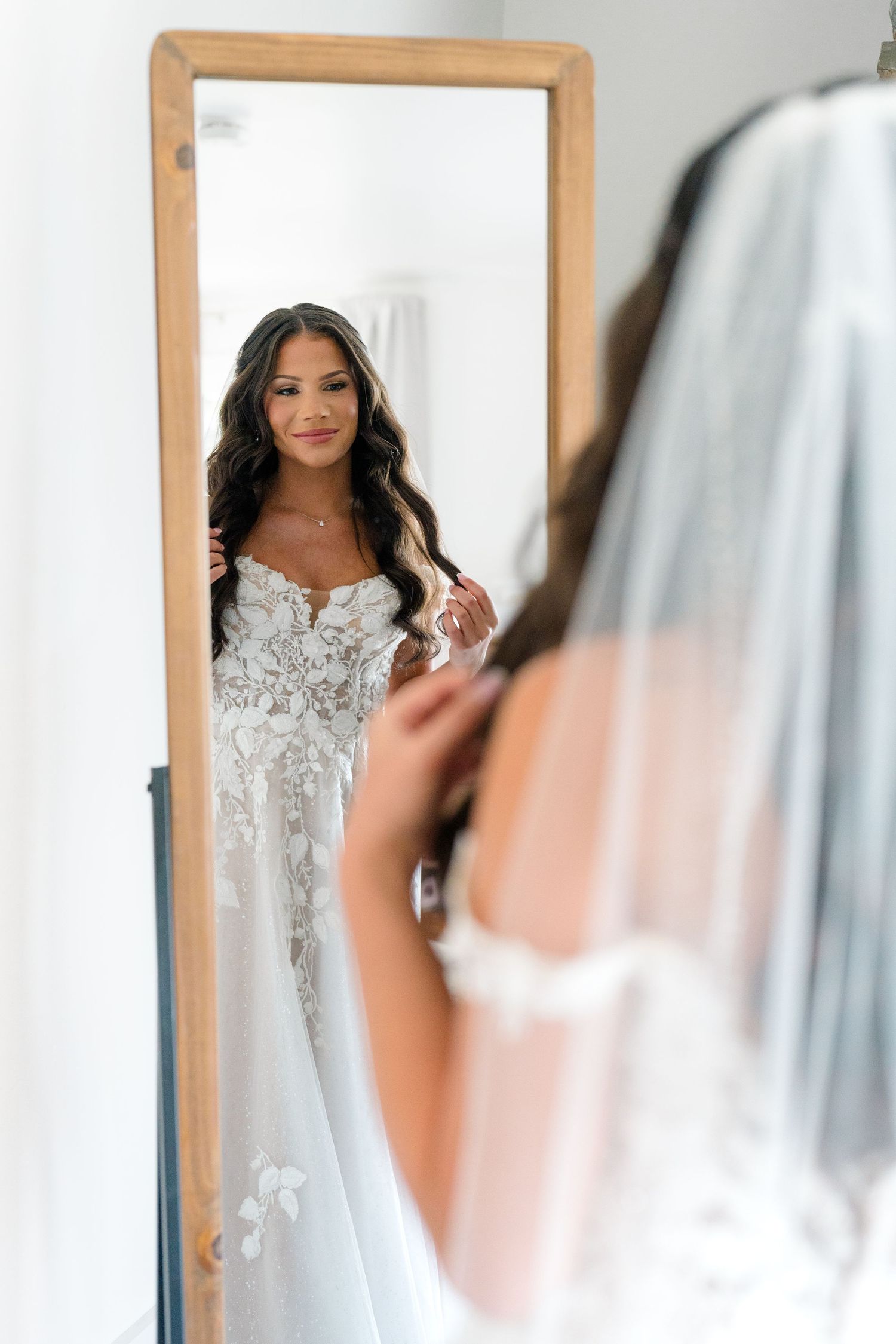 Reflection of bride in white lace gown looking in mirror during wedding preparations.