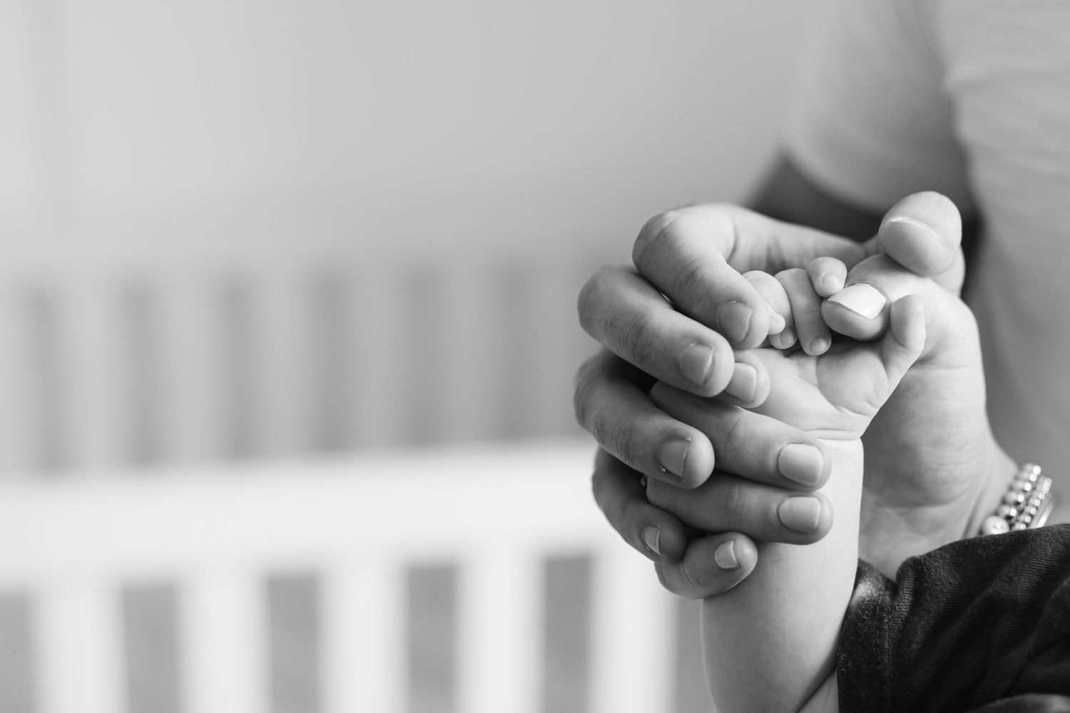 Black and white close-up of tiny baby fingers grasping an adult's finger, showing tender connection and care.