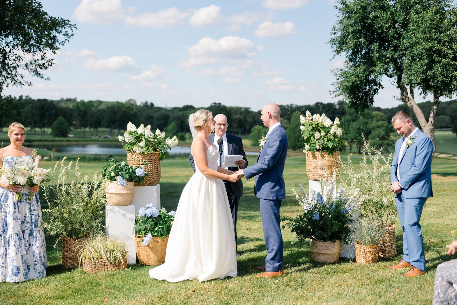 A bride and groom exchange vows at an outdoor ceremony with white floral arrangements.