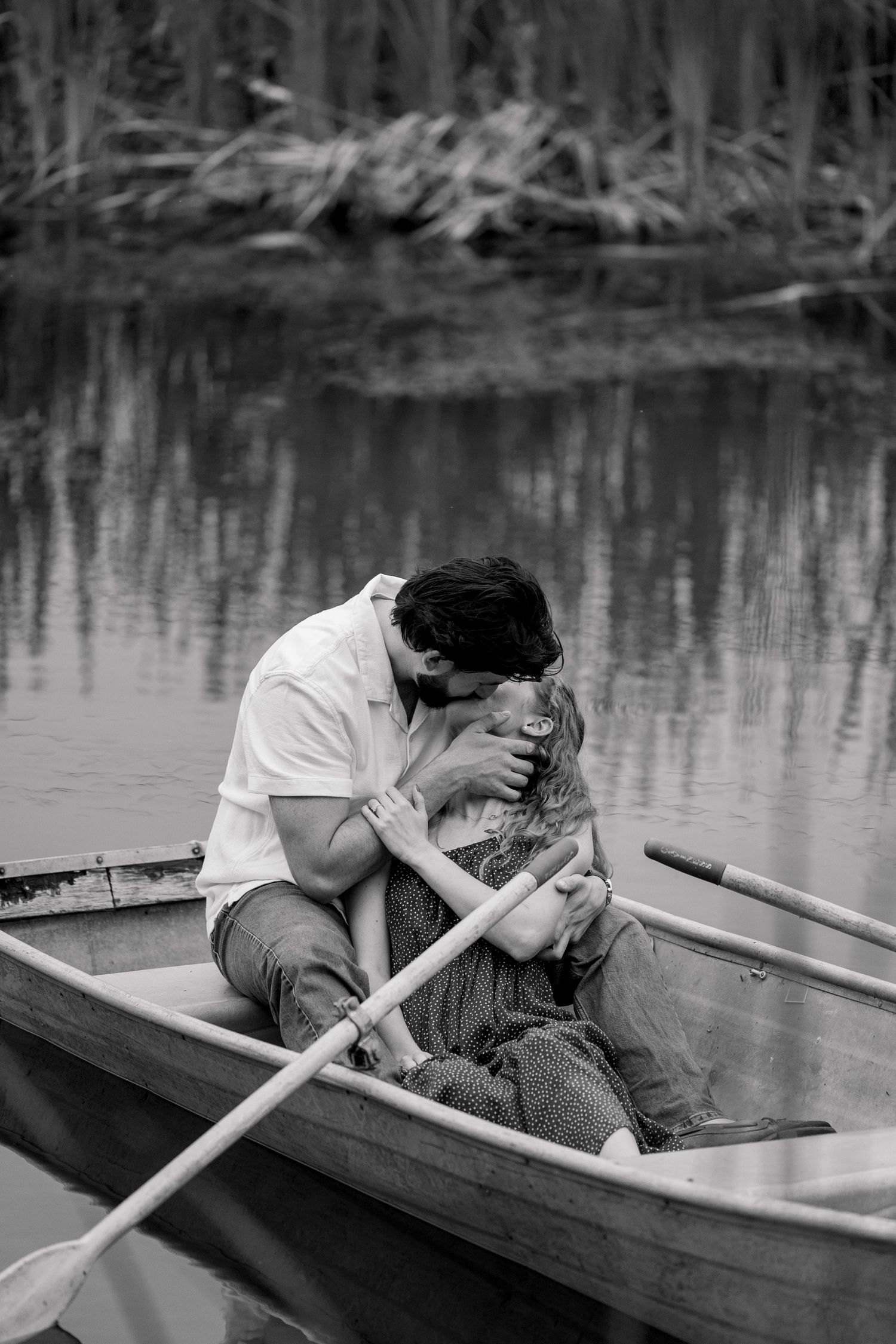 A black and white photo series shows two people embracing intimately in a wooden rowboat on still water.