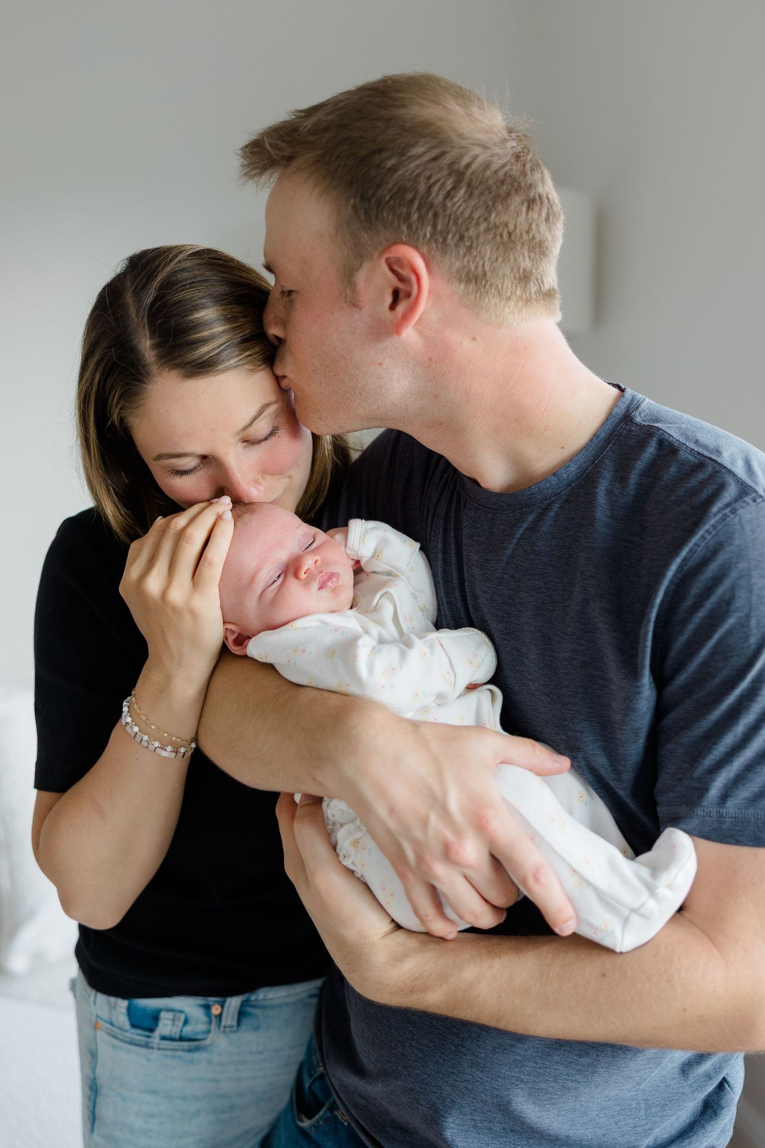 Family shares intimate moment together with newborn baby in white onesie.