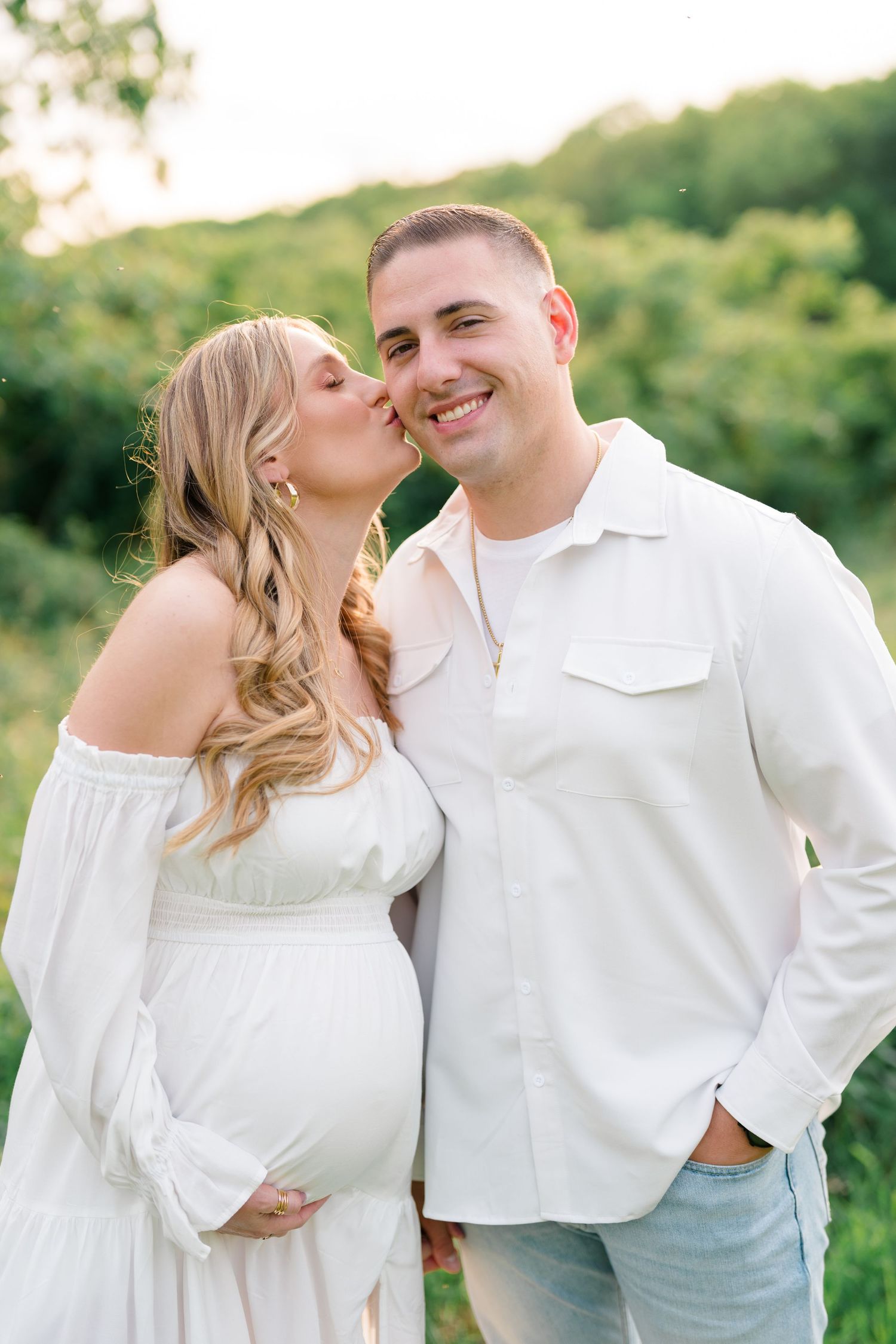 Romantic maternity session featuring couple in white clothing sharing intimate moments outdoors.