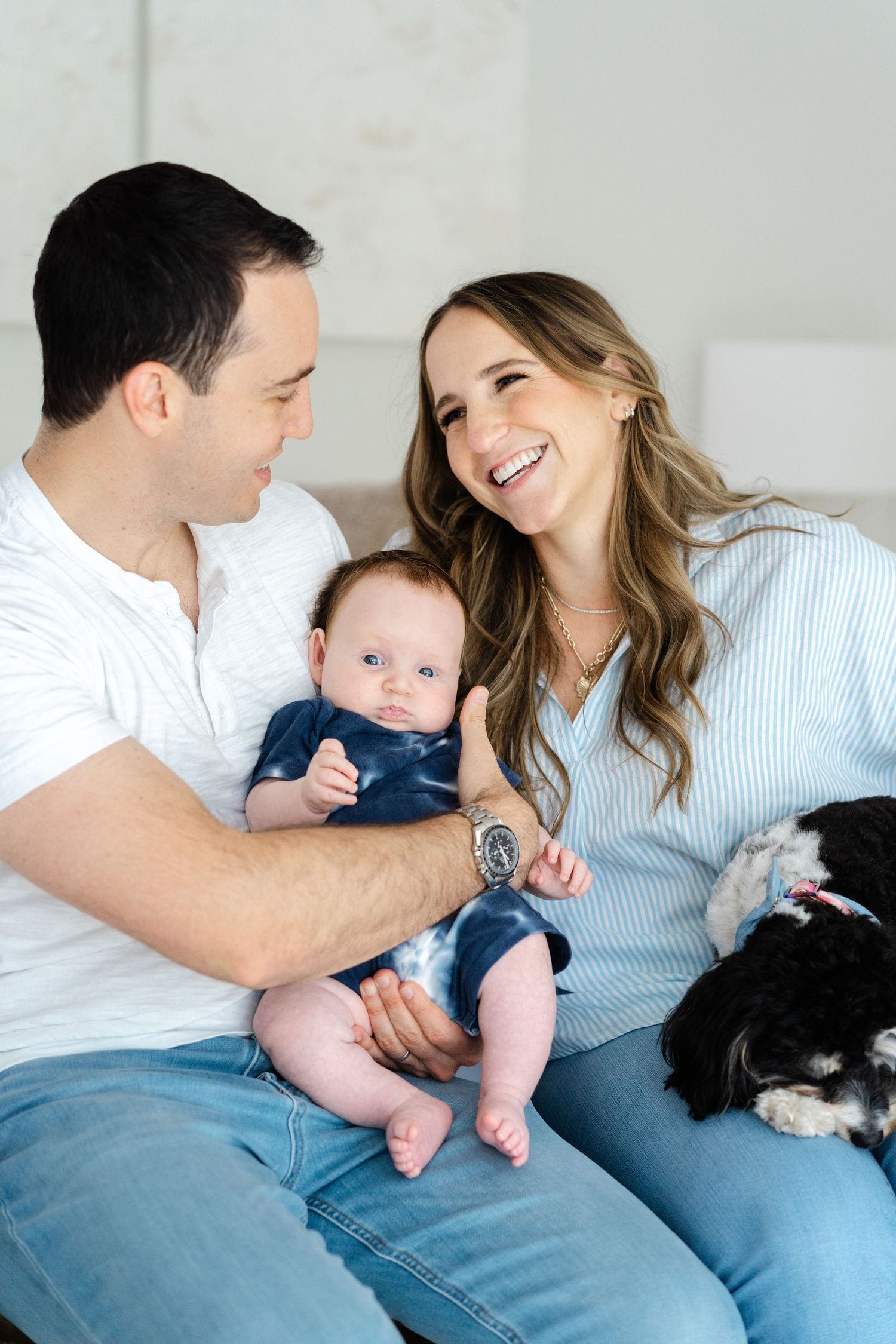A couple shares a joyful moment with their baby and dog while relaxing on a bench at home.