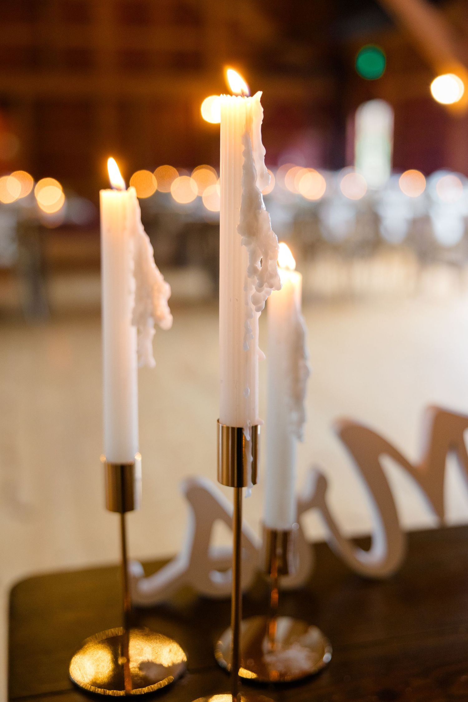 White taper candles glowing in gold holders at wedding reception.