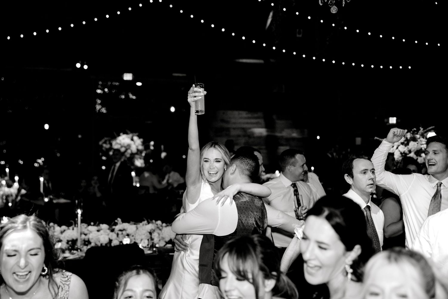Black and white photo of wedding reception dance floor with string lights overhead.