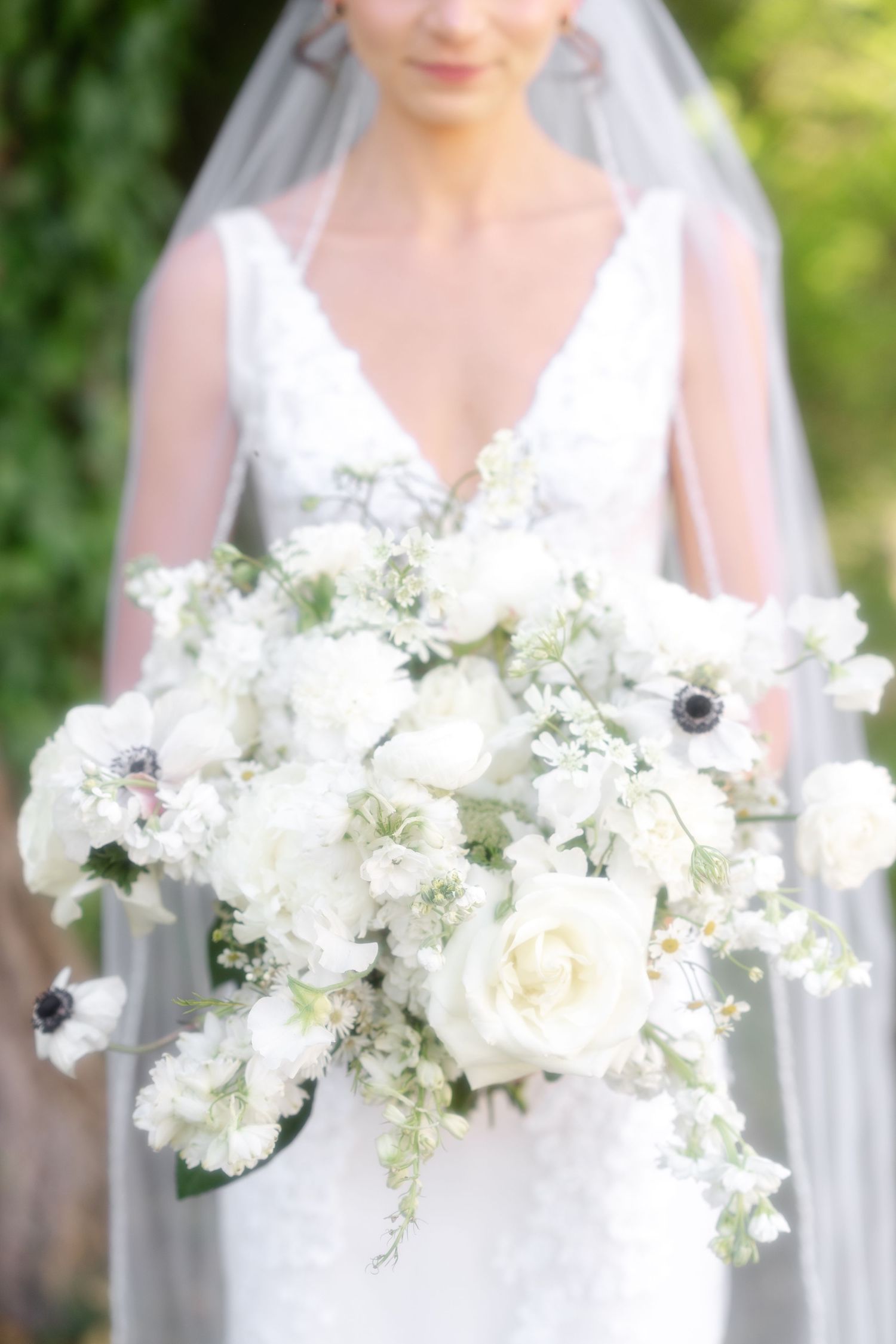 A collection of delicate white and ivory wedding bouquets arranged in elegant glass vases against a sunlit garden background.